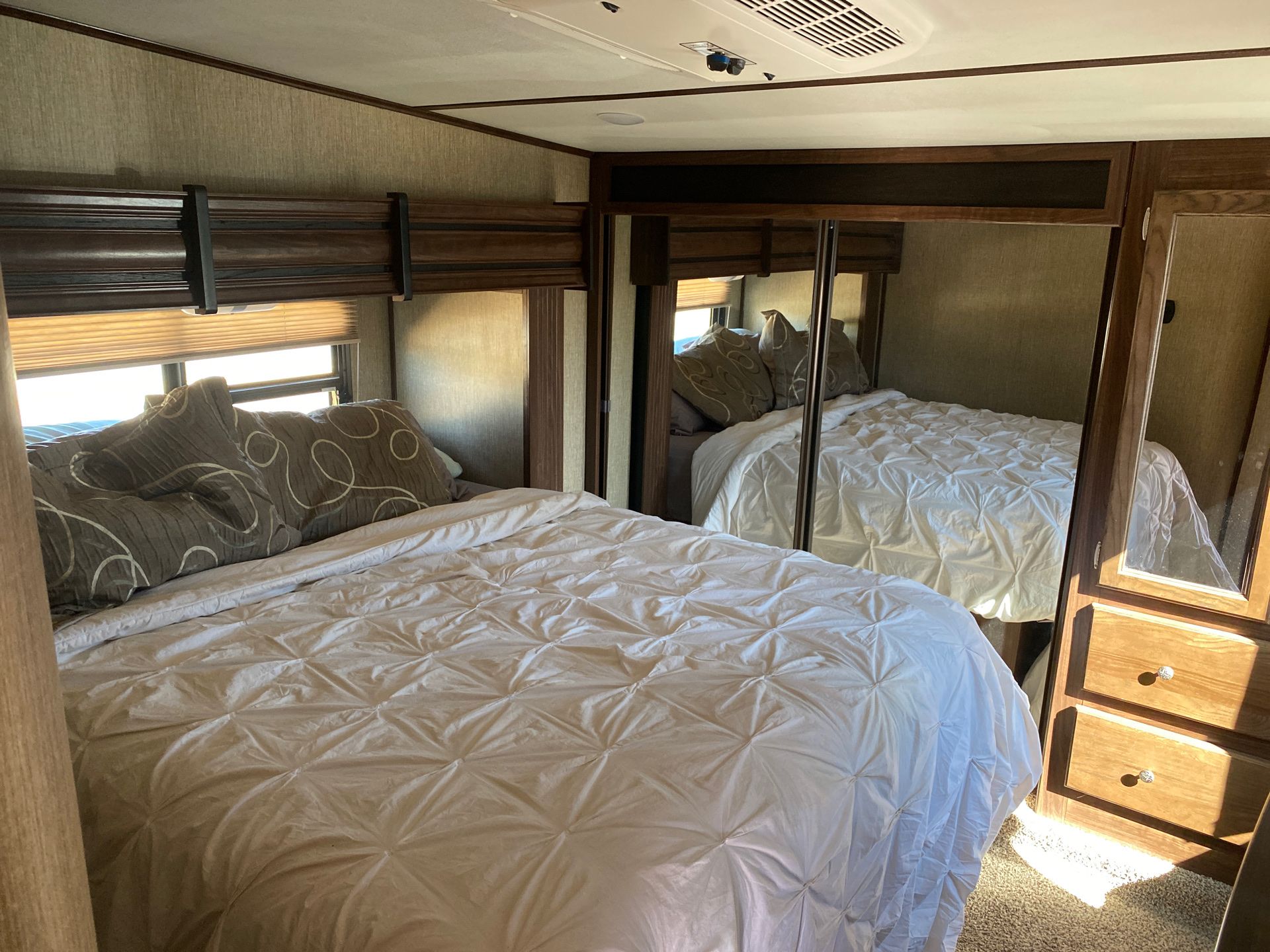 Spacious RV rental bedroom with a comfortable bed, window blinds, and mirrored wardrobe for restful travel.. Keystone RV Sprinter 2017