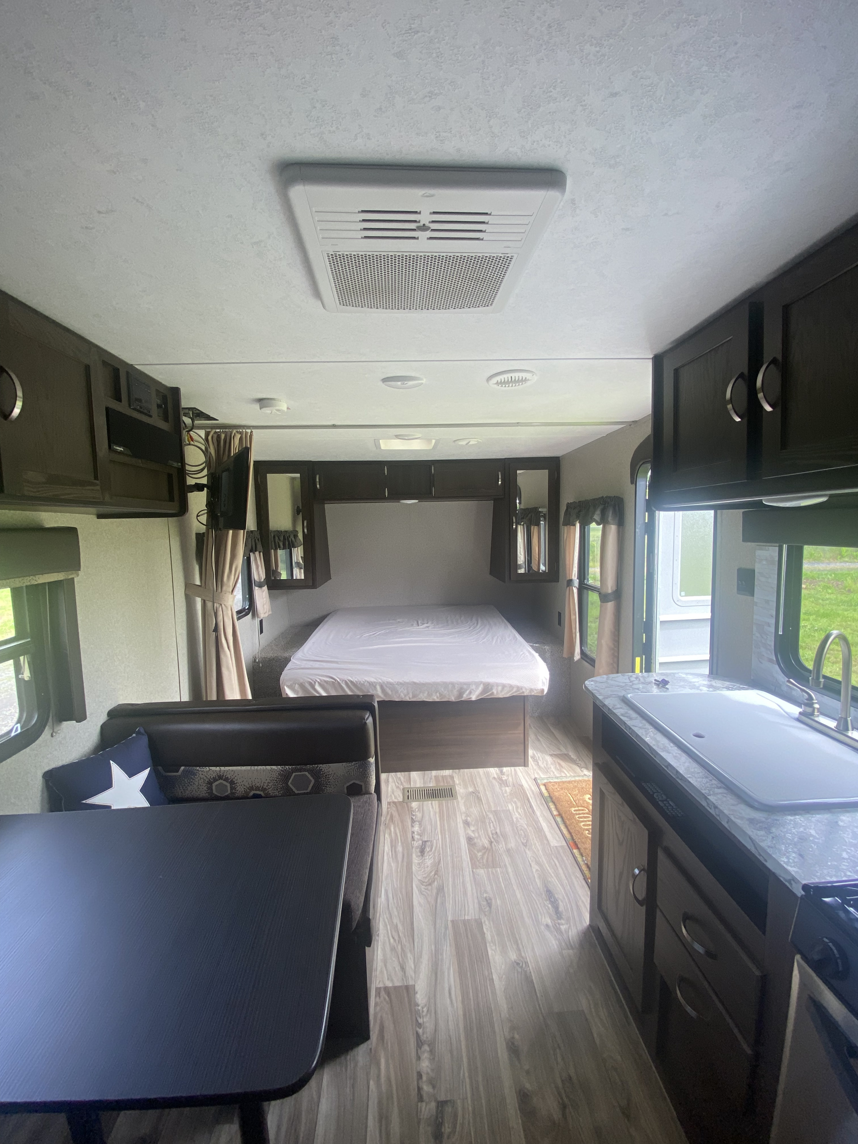 RV rental interior view: comfortable bed in the rear, dining booth, and fully-equipped kitchen with sink, all on wood-look flooring.. Keystone RV Springdale 2018