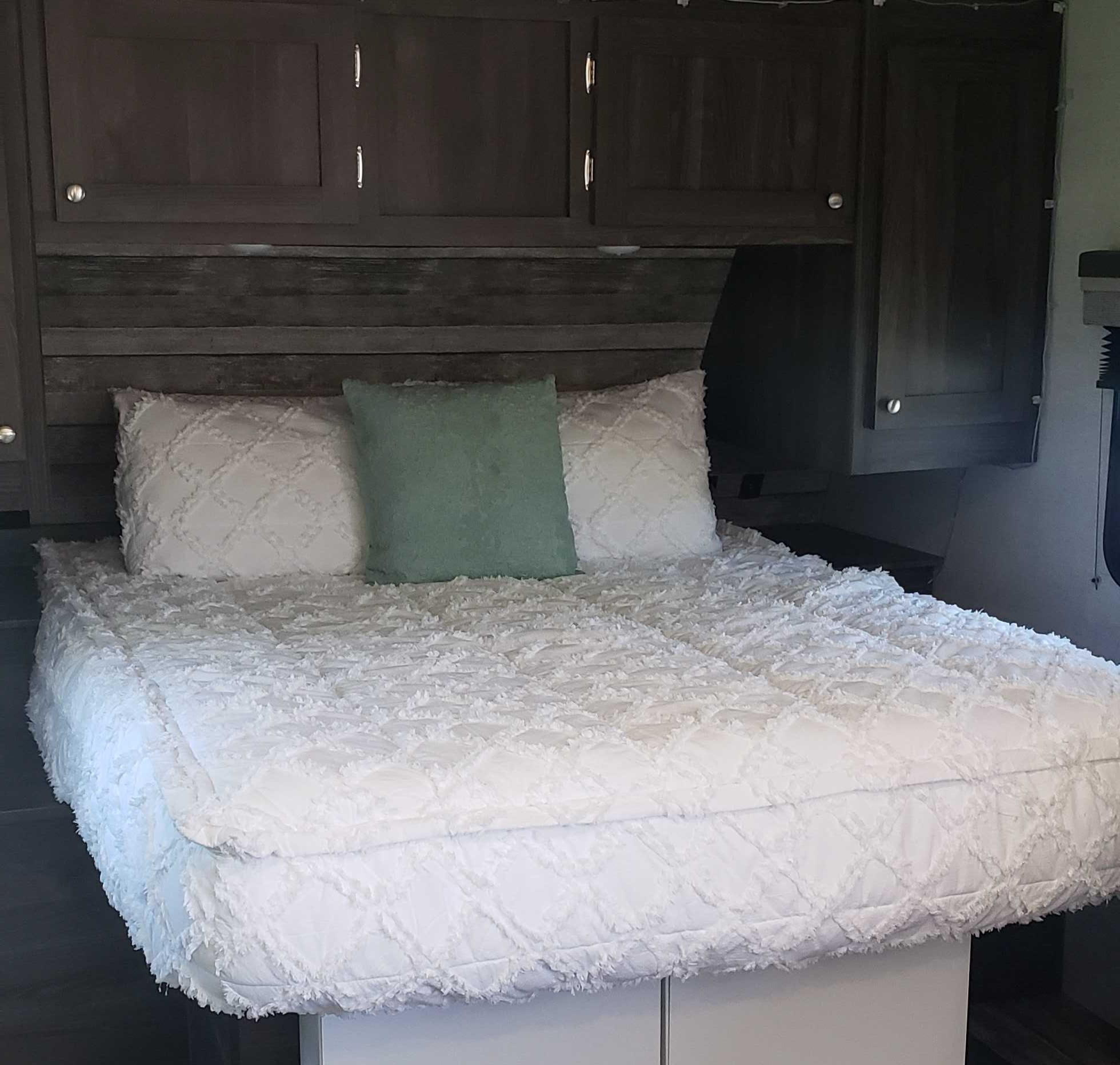 Cozy RV rental bedroom featuring a comfy white bed, green accent pillow, and dark wood overhead cabinets.. Starcraft Super Lite 2020