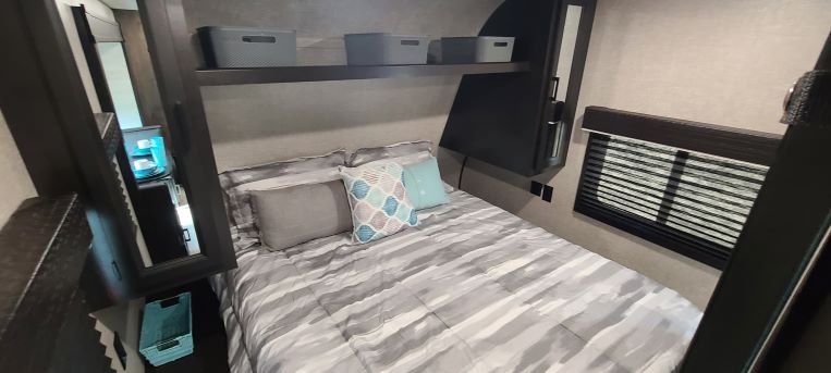 Inside an RV rental: a compact bedroom features a bed with striped bedding, throw pillows, and built-in storage.. Jayco Flight 242BHS 2022