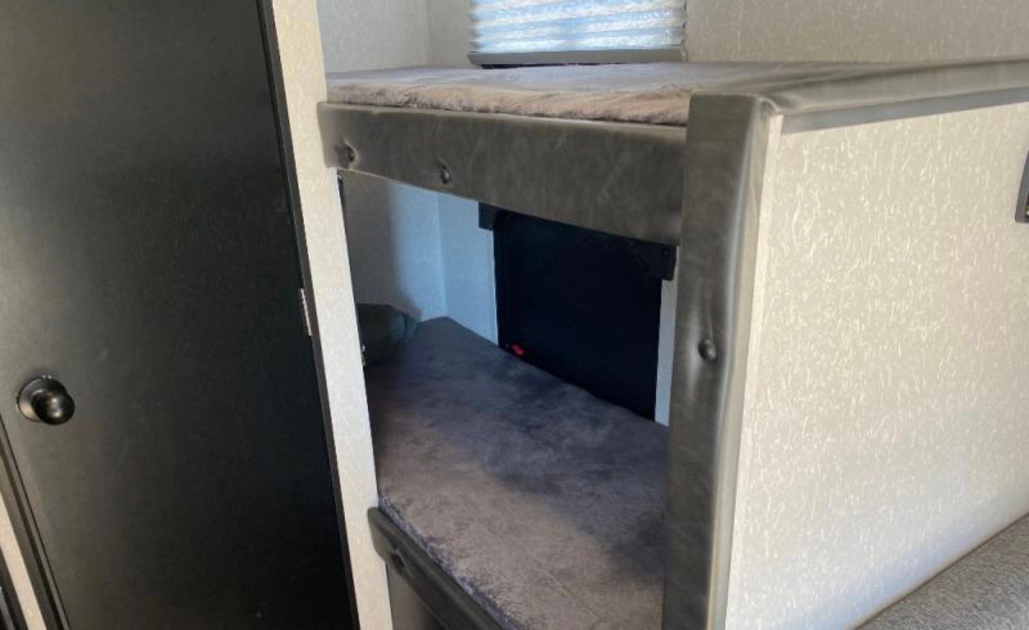 Interior of an RV rental showing two gray bunk beds, a black door, and a window. Perfect for family adventures.. Forest River Cherokee Wolf Pup 2022