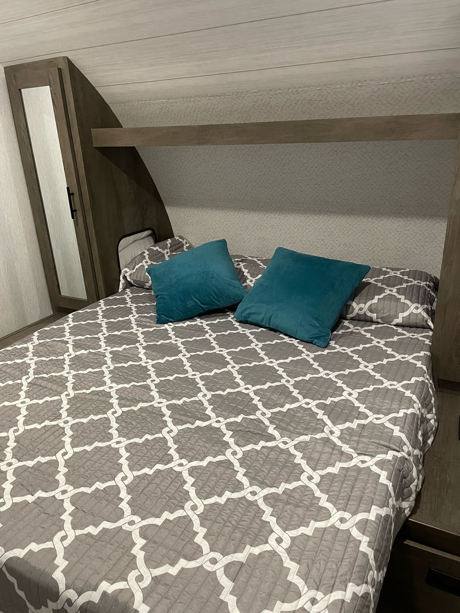 Step into comfort! This RV rental bedroom features a gray & white patterned bedspread, teal pillows, and built-in storage with a mirror.. Forest River Other 2022