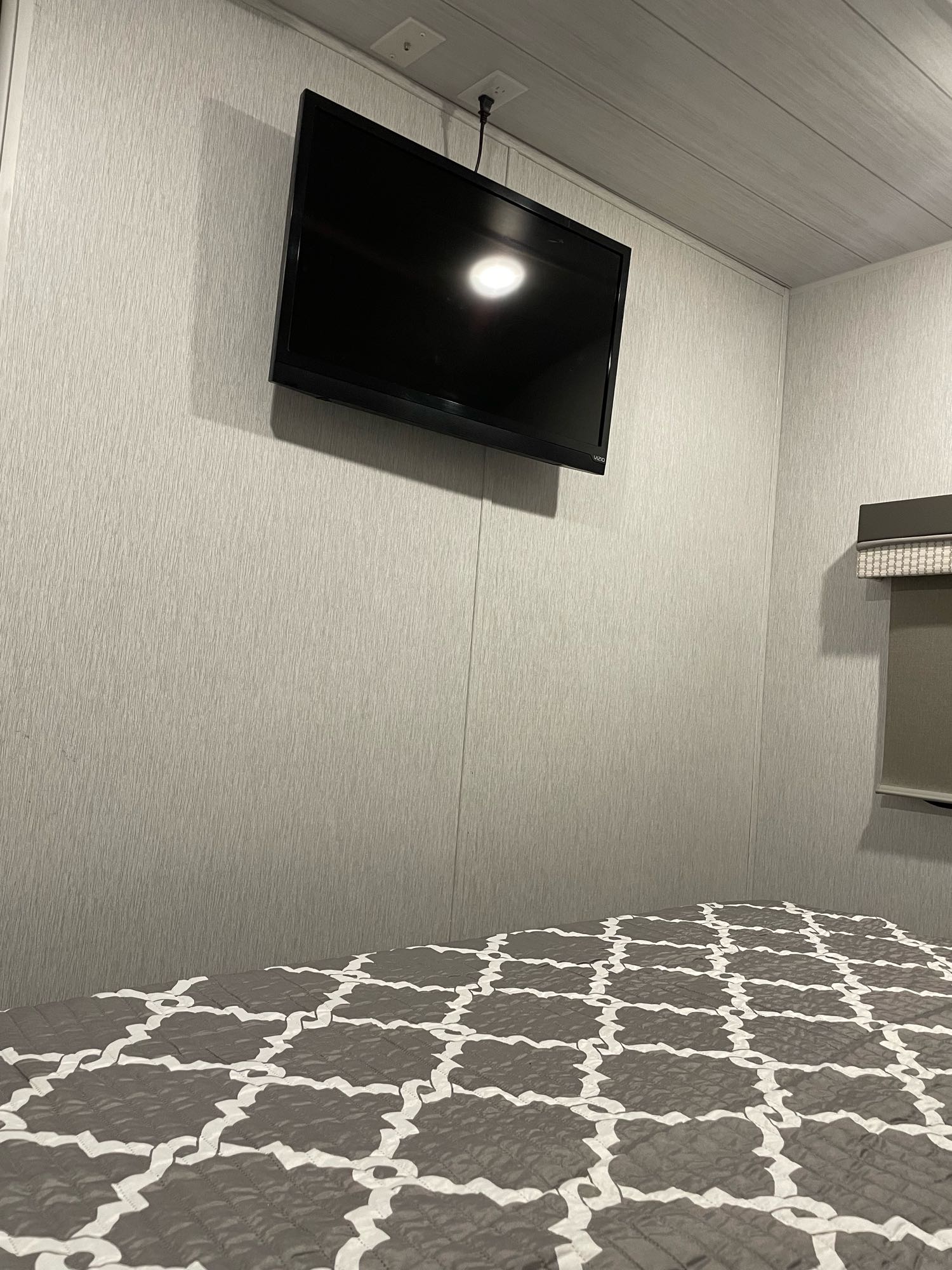 Inside a modern RV rental: mounted TV, light gray textured walls & ceiling, and a comfy patterned bed.. Forest River Other 2022