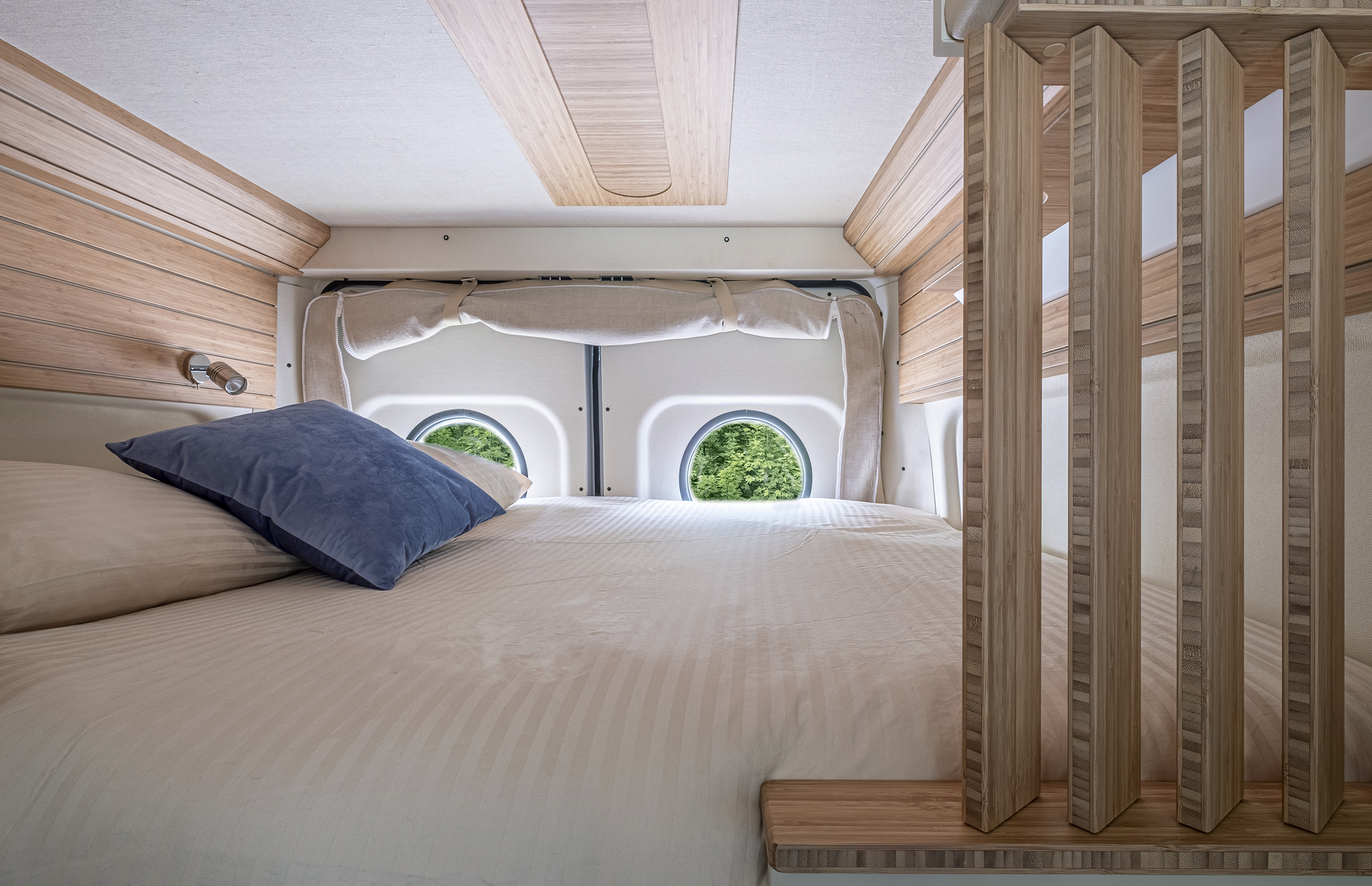 Relaxing RV rental bedroom with striped bedding, a blue pillow, warm bamboo paneling, and unique round windows.. Fiat Ducato MH2 2020