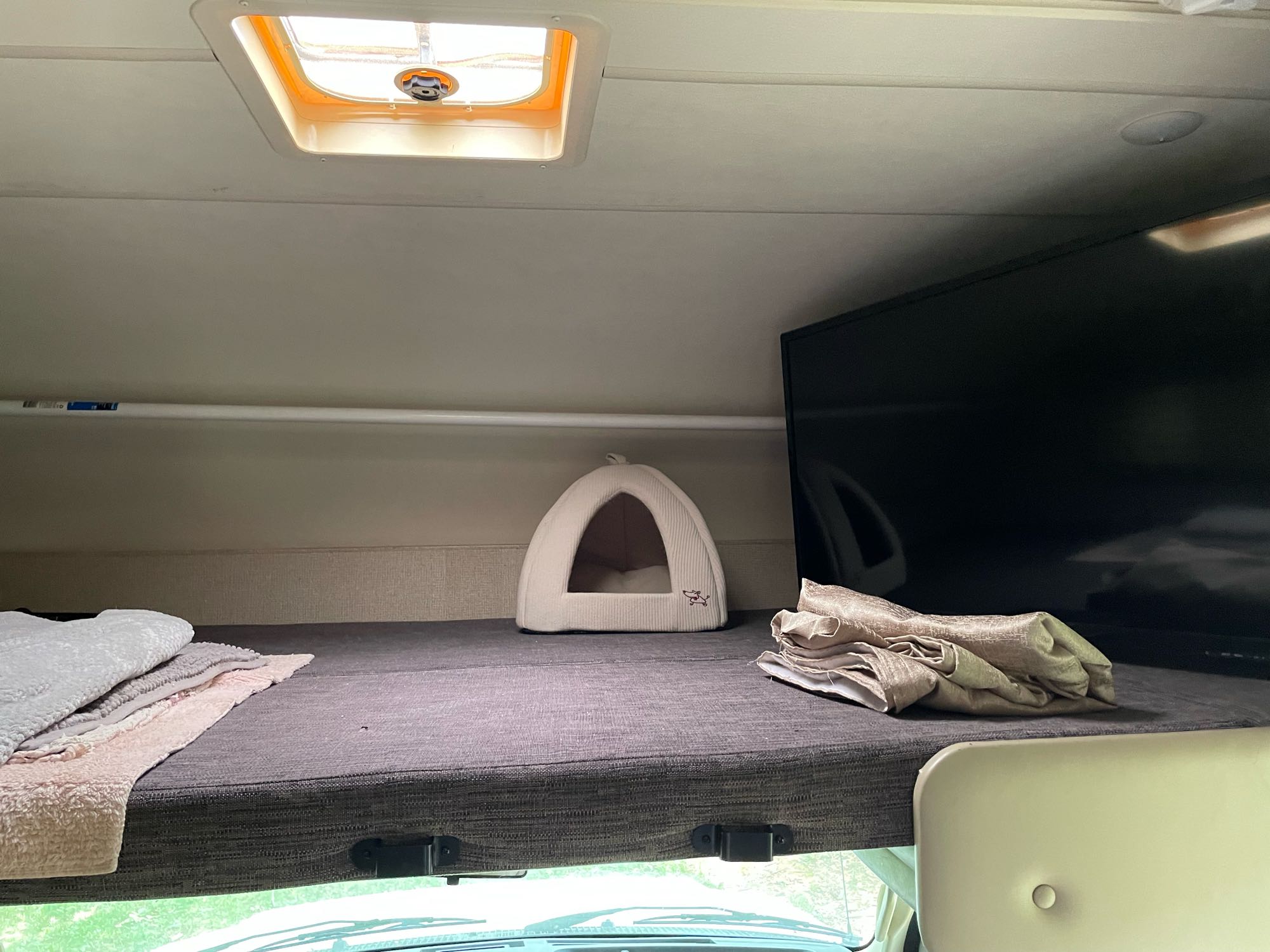 Cozy rv rental overhead bunk: pet bed, folded blankets, and mounted TV. Ready for comfortable travel adventures.. Thor Four Winds 2018