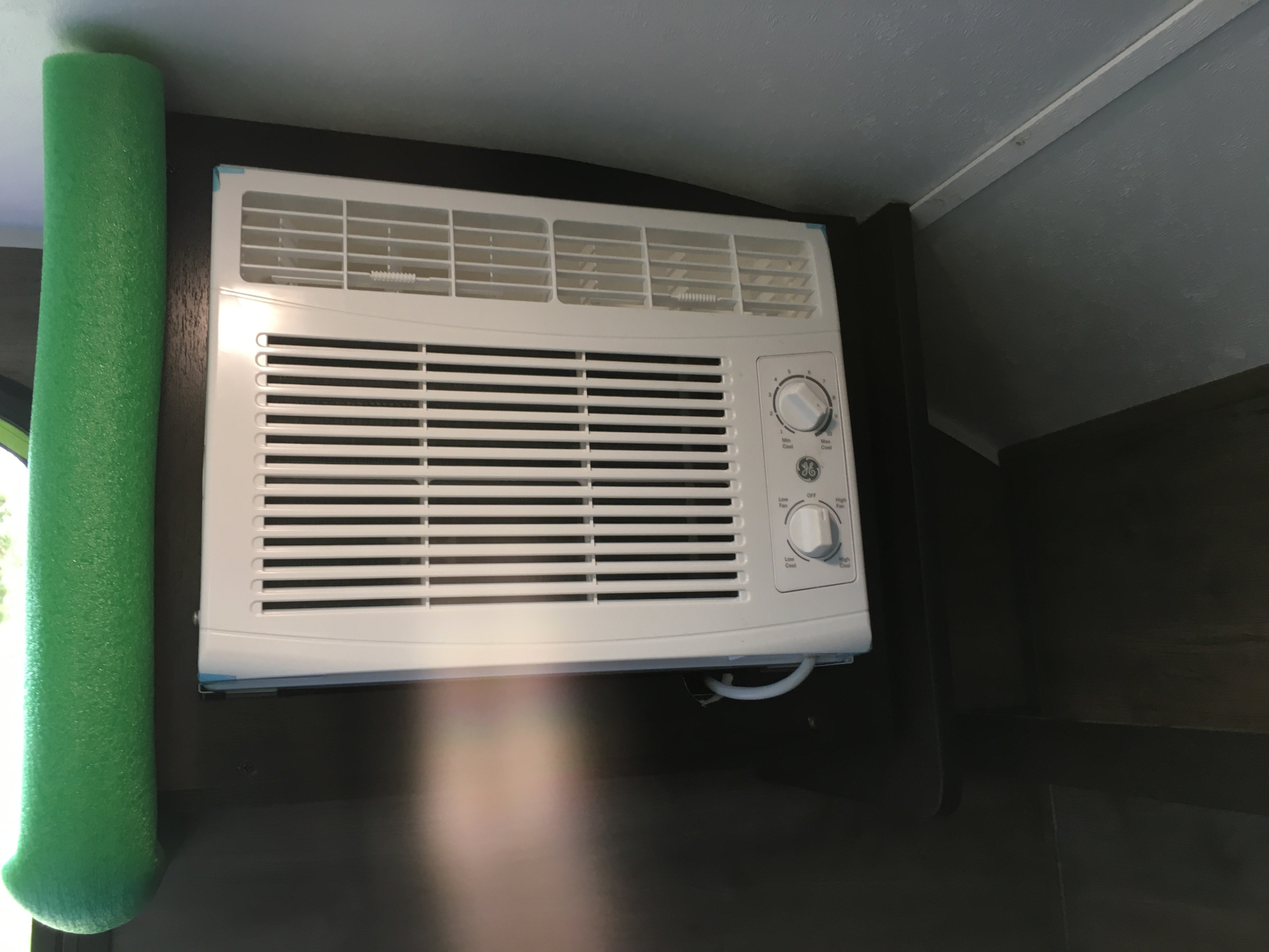 White GE air conditioner with control knobs and green foam insulation, seen inside an RV rental for cooling comfort.. Braxton Creek Bushwhacker 2021