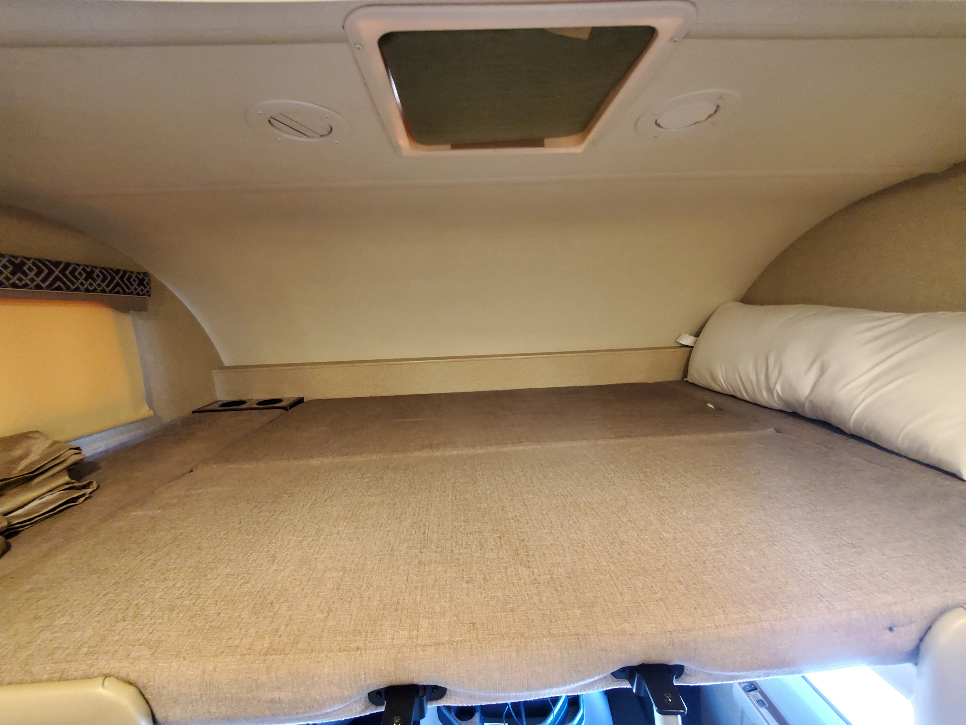 RV rental overhead bunk bed features a mattress, pillow, window, cup holders, and ceiling skylight/vents, ready for rest.. Thor Motor Coach Four Winds 2019