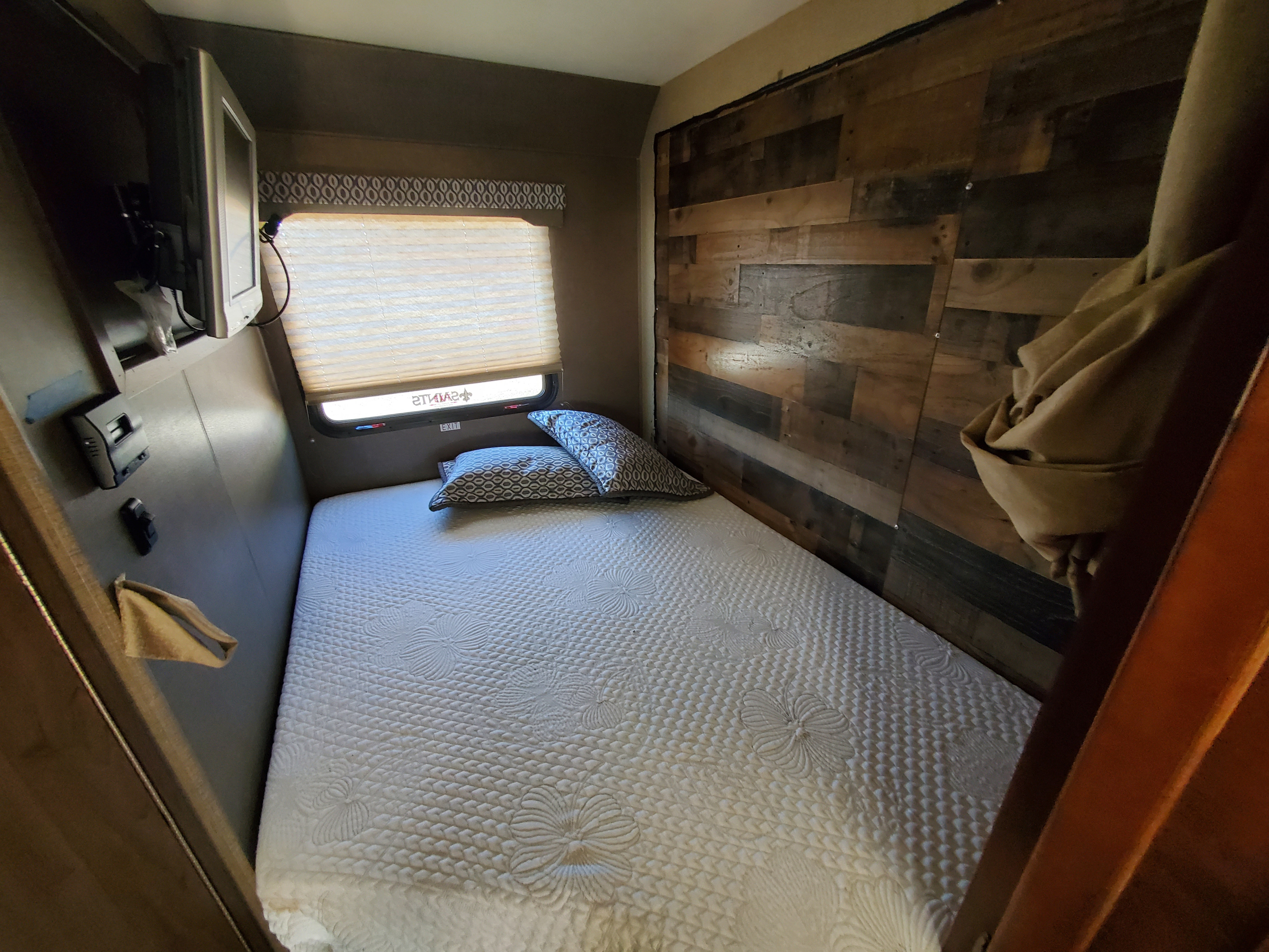 Cozy RV rental bedroom with a comfy bed, mounted TV, and stylish wooden accent wall. Perfect for a restful night.. thor freedom elite 2019