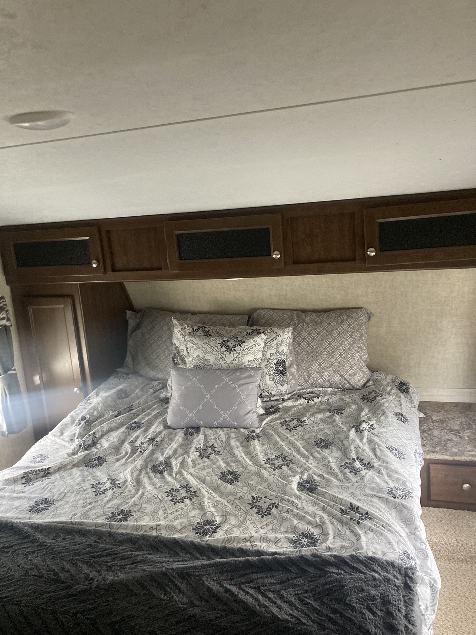 Comfortable RV rental bedroom featuring a bed with patterned linens, pillows, and overhead cabinets.. Keystone RV Hideout 2016