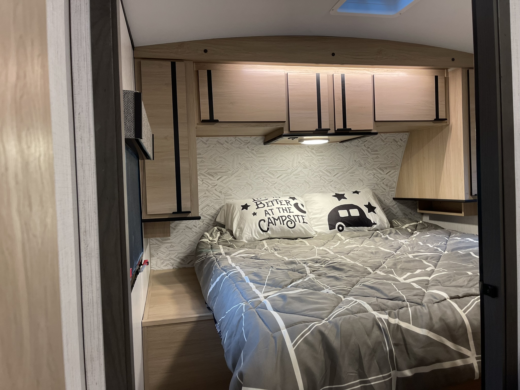 This cozy **RV rental** features a comfortable **bedroom** with a bed, geometric wallpaper, and smart overhead storage.. Cruiser RV Radiance 2022
