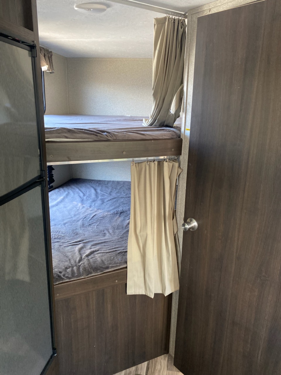 RV rental interior featuring two bunk beds with bedding and privacy curtains; a door is seen right.. Keystone RV Springdale 2020