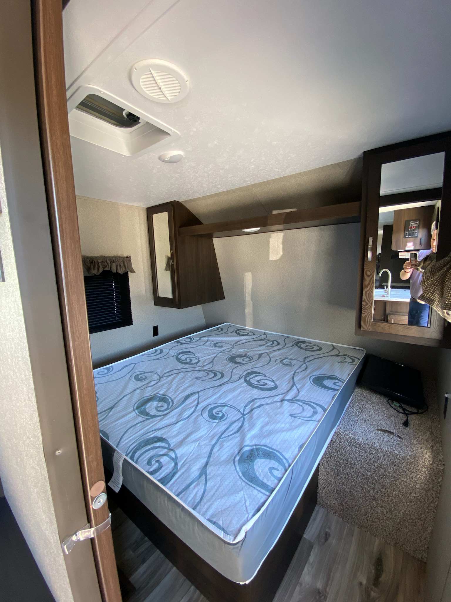 RV rental bedroom: a compact space featuring a patterned bed, window with blinds, and mirrored overhead storage.. Keystone RV Springdale 2020
