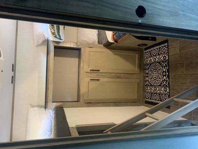 RV rental interior with bunk beds: two sleeping levels, a ladder, and light wood storage cabinets with a patterned rug.. Forest River Cherokee Alpha Wolf 2022