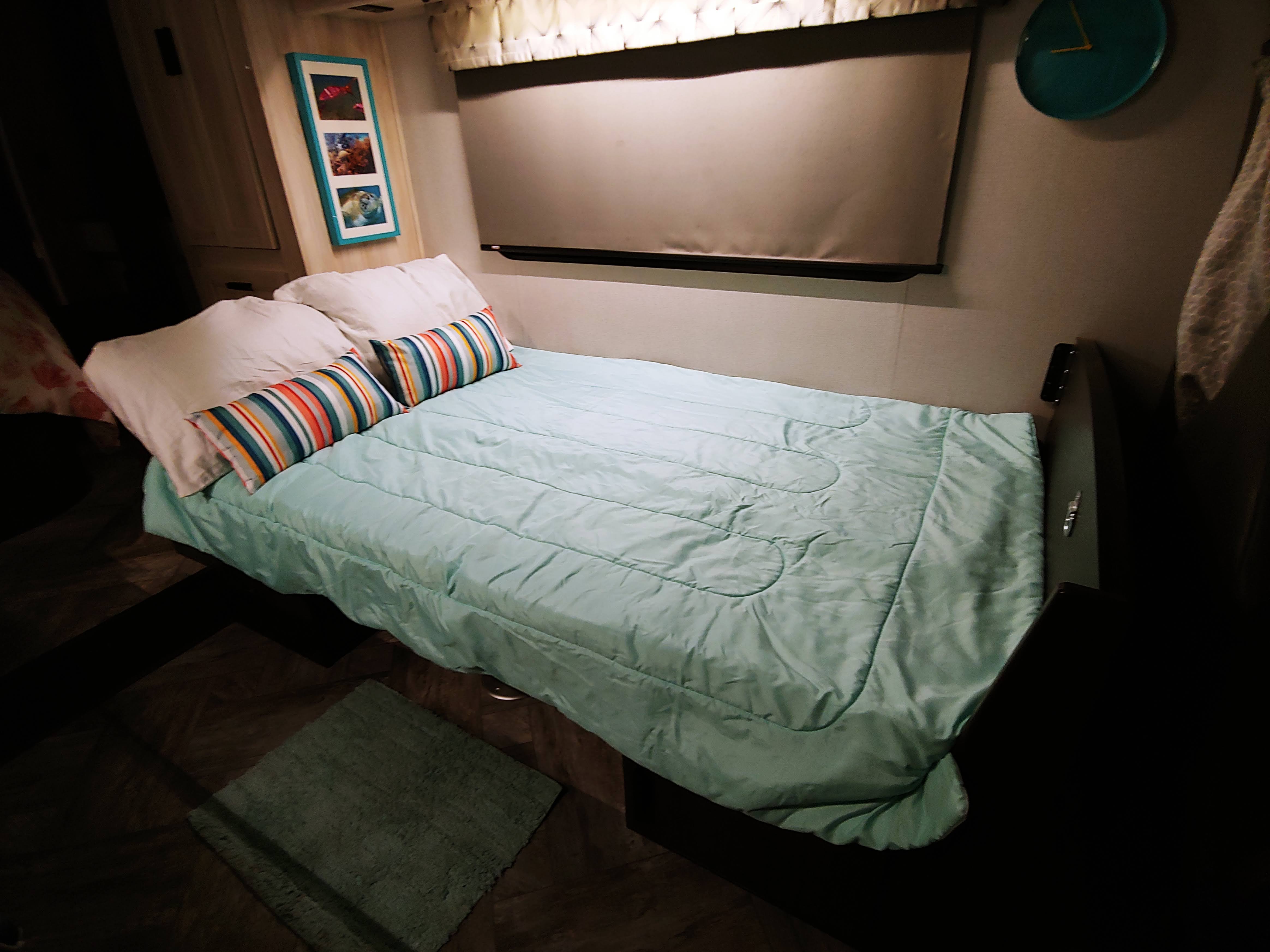 RV rental bedroom with a light blue bed, striped pillows, teal decor, and wood floors.. Forest River Sunseeker 2350LE 2022