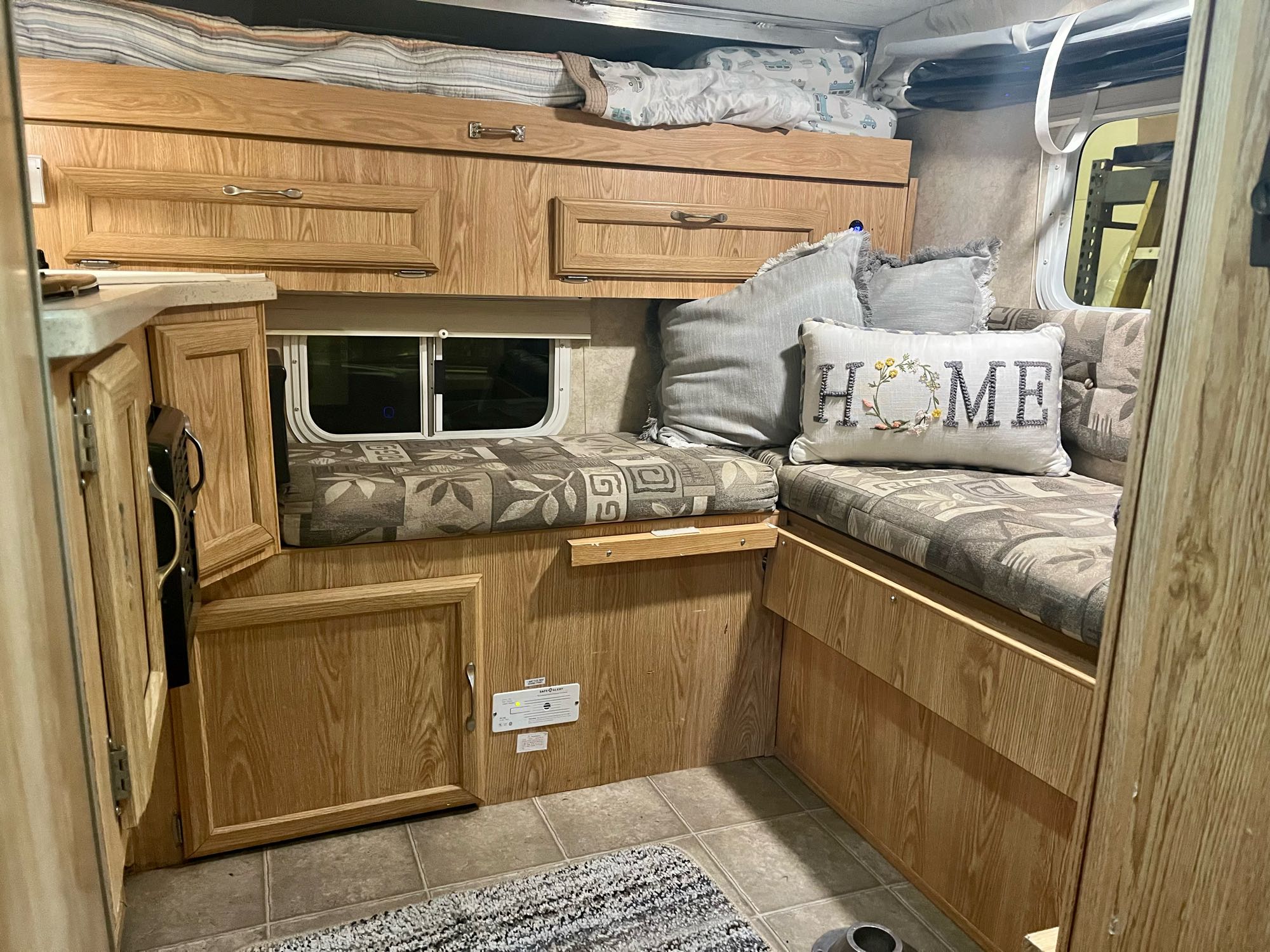 Inside an RV rental, showing a cozy dinette area with light wood cabinets, patterned cushions, and an overhead bunk.. Ford F350 Diesel Double Cab 2004