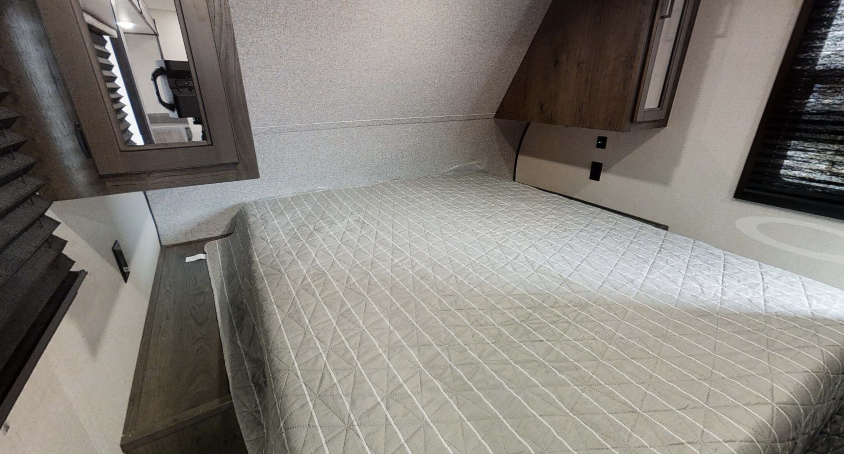 RV rental bedroom: Cozy space with a gray quilted bed, wood cabinets, and a mirrored side vanity.. Starcraft Autumn Ridge 2022