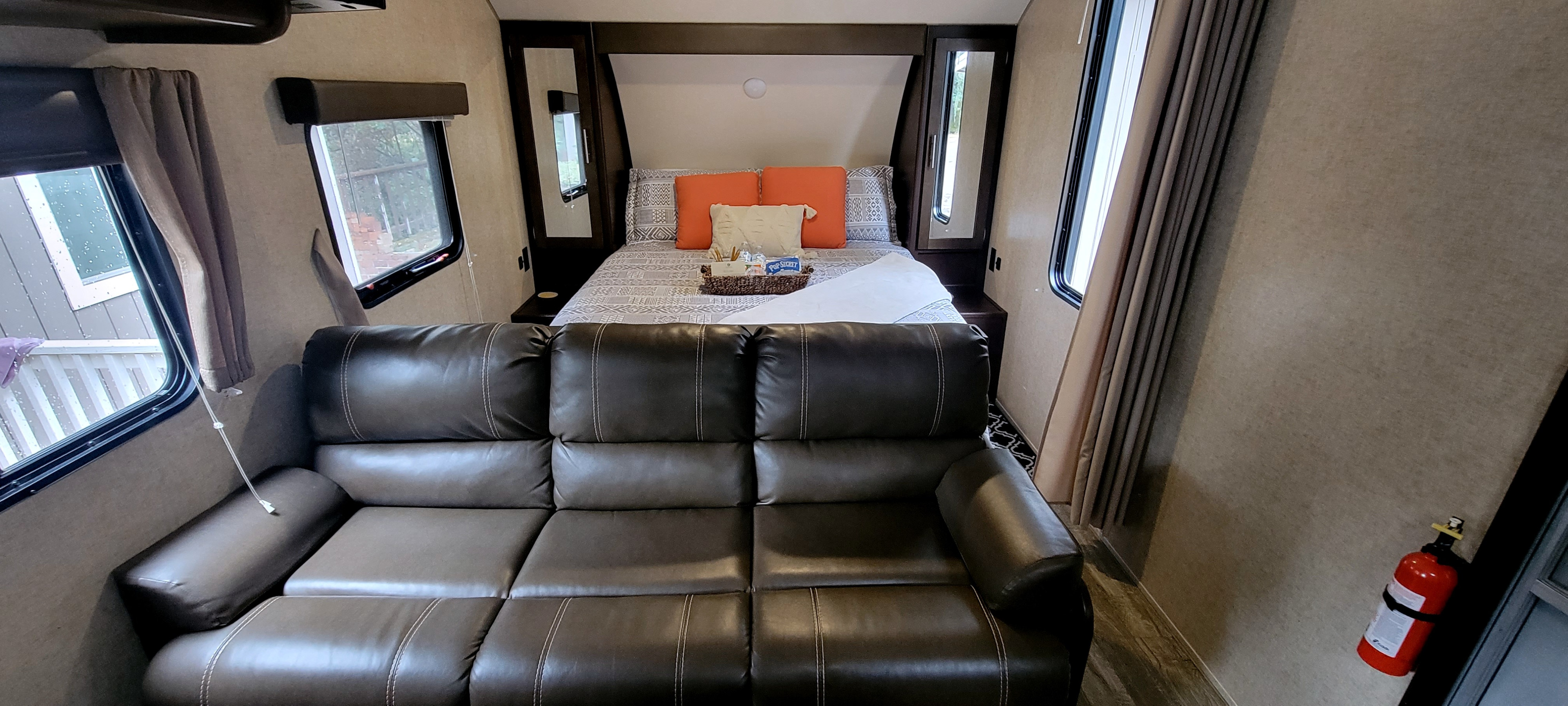 Interior view of an RV rental, showing a large brown sofa, queen-sized bed, and fire extinguisher.. Forest River Cherokee Grey Wolf 2018