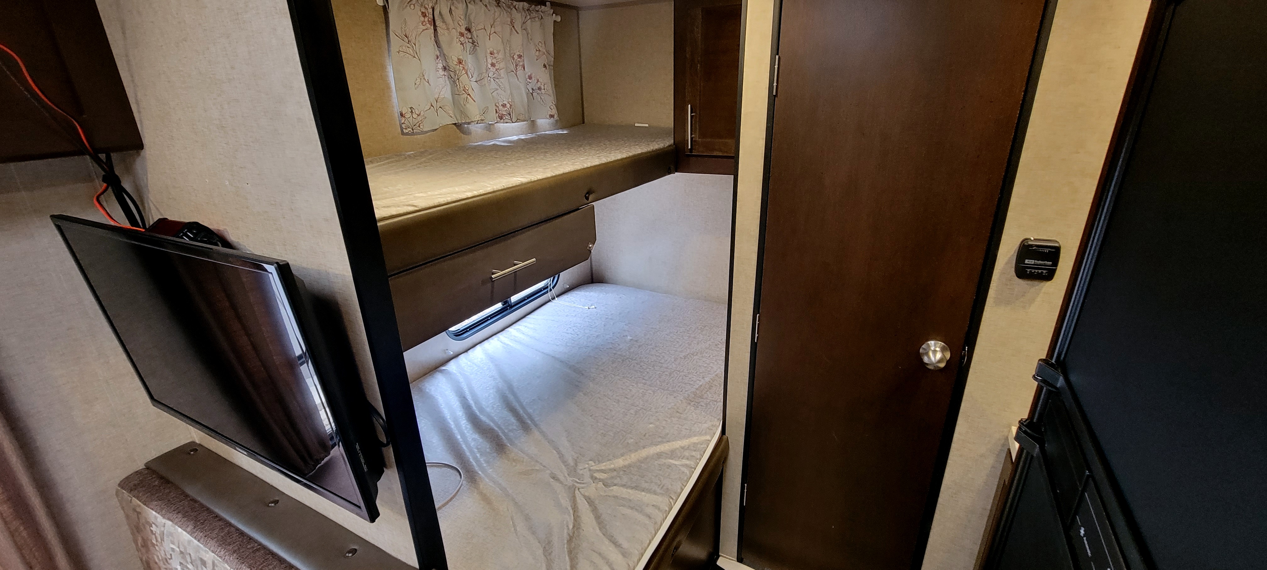 Inside an RV rental: upper and lower bunk beds with mattresses, a TV, and a door, providing cozy sleeping space.. Forest River Cherokee Grey Wolf 2018