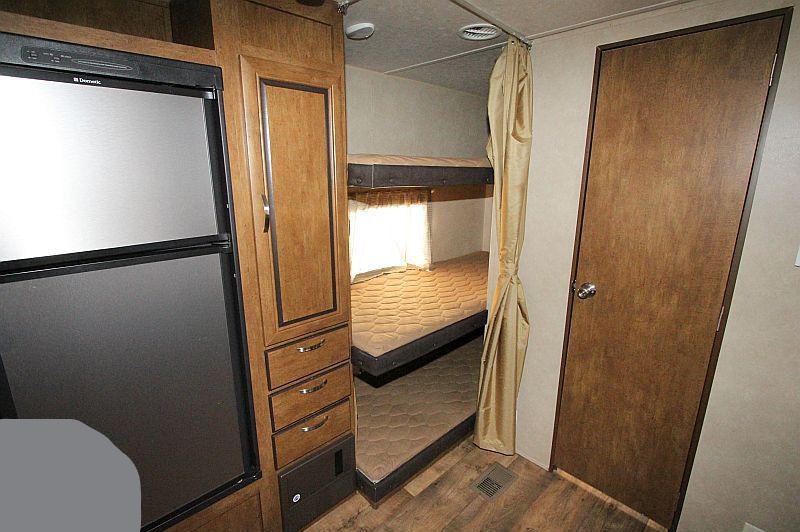 View inside an RV rental showing the Dometic fridge, cabinetry, and bunk beds with a privacy curtain.. Forest River Salem 2017