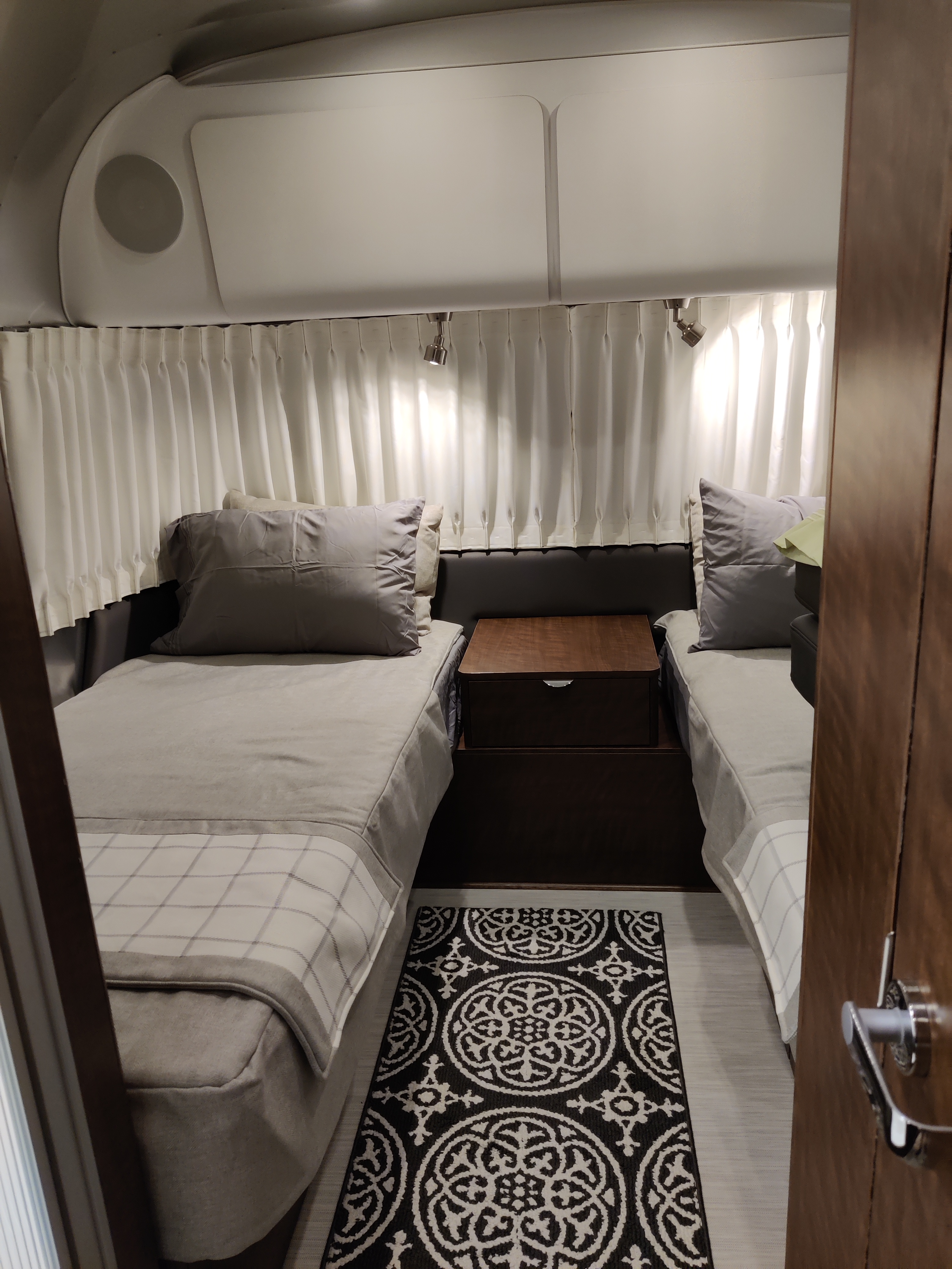Cozy RV rental bedroom: two beds, overhead storage, white curtains, and a striking black-and-white patterned rug.. Airstream Globetrotter 2021