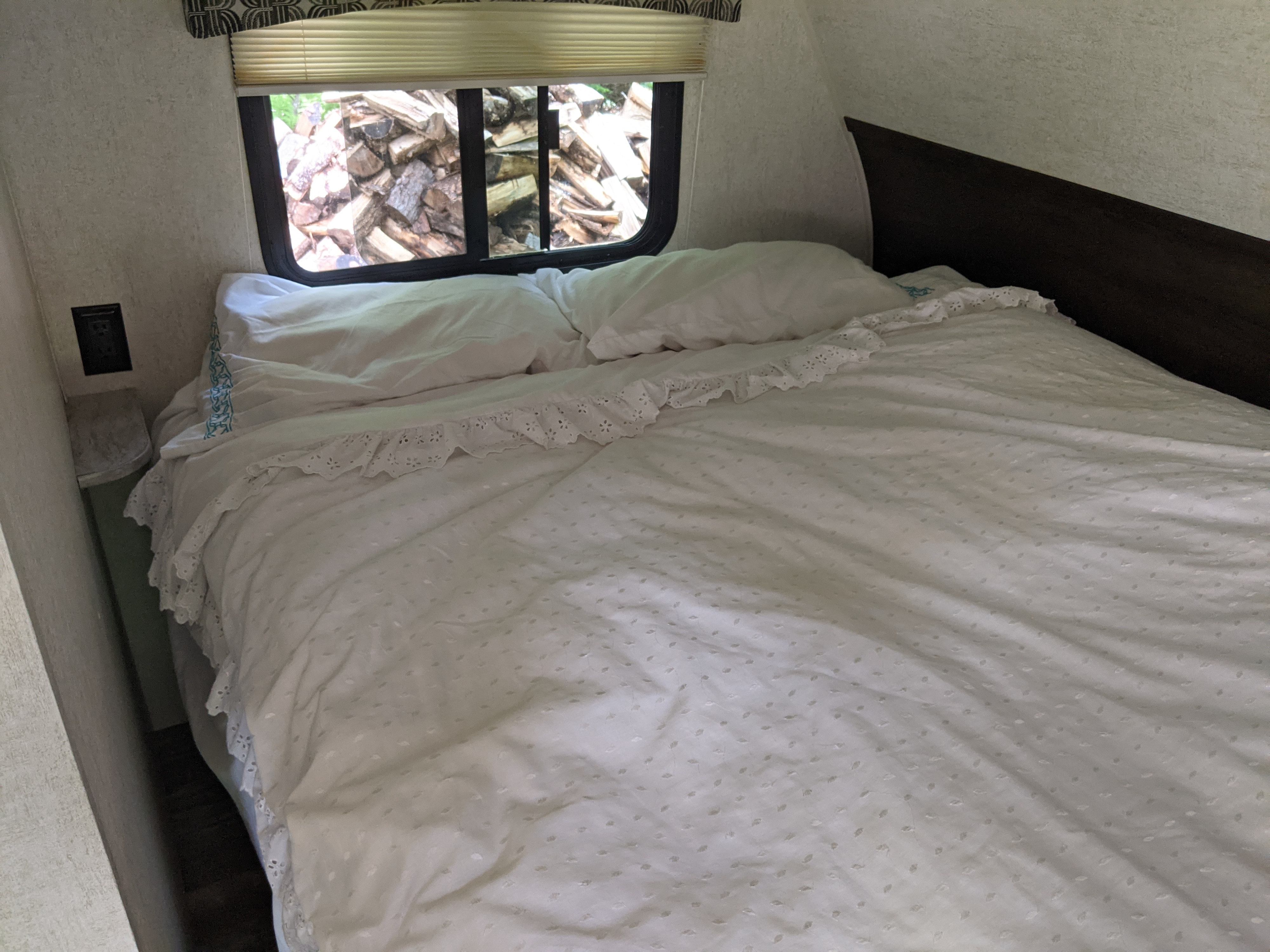 Relax in this cozy RV rental bedroom with a white bed, ruffled bedding, and a window view of stacked firewood.. Starcraft Autumn Ridge Outfitter 2019