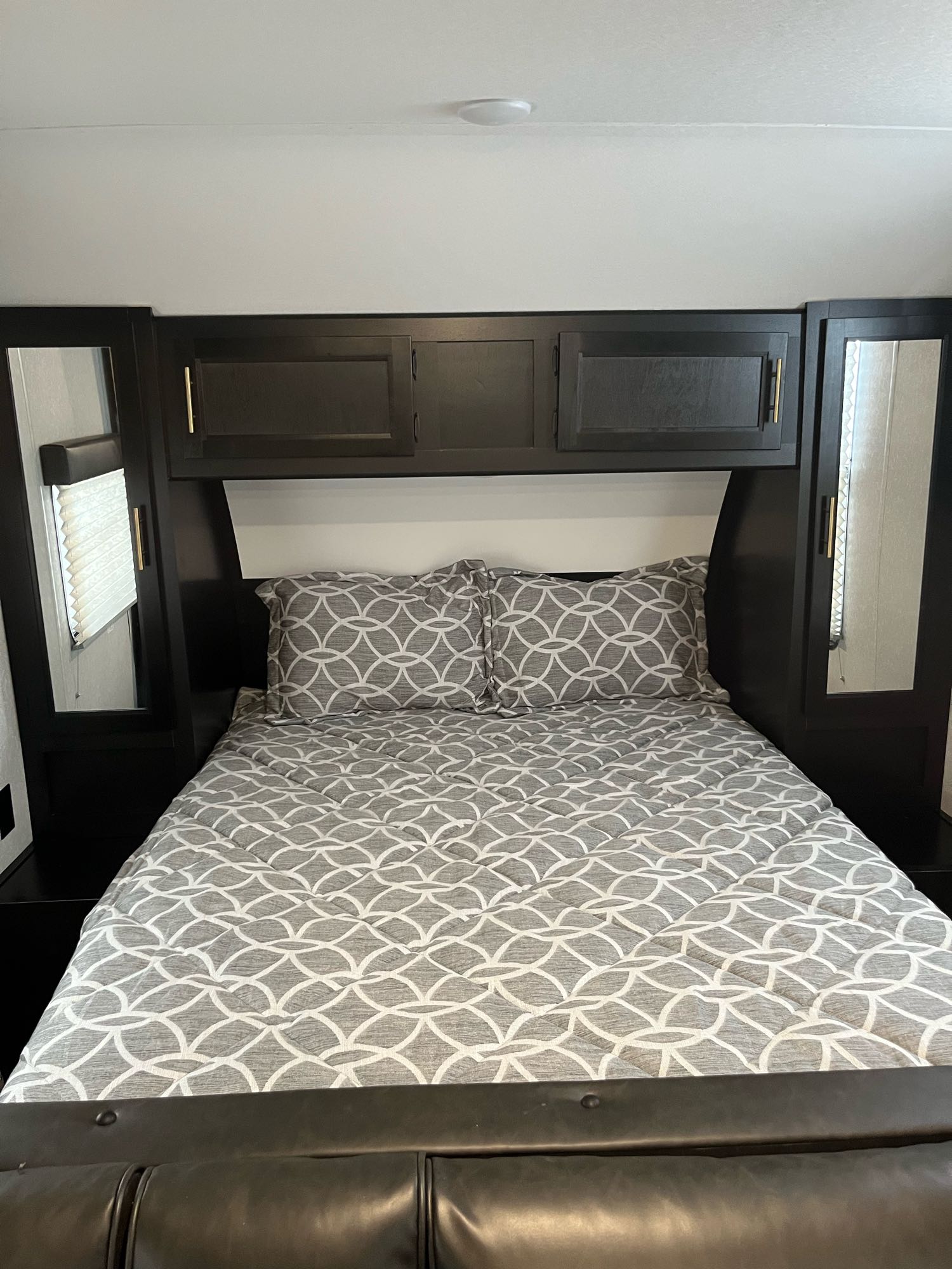 RV rental bedroom interior: a comfortable bed with gray patterned bedding, flanked by dark cabinetry and mirrors.. Forest River Cherokee Grey Wolf Special Edition 2022