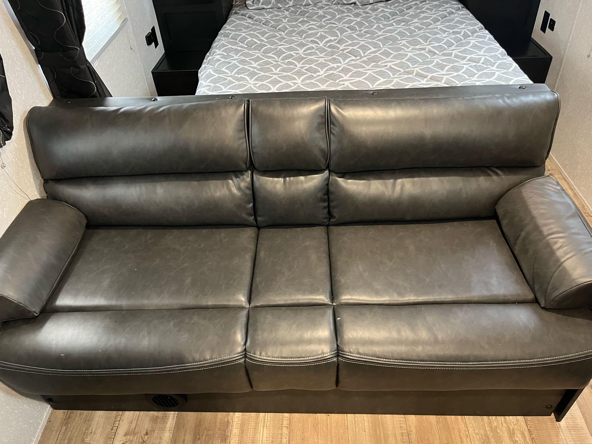 Inside an RV rental: a dark gray sofa with white stitching offers seating, with a bed visible in the background.. Forest River Cherokee Grey Wolf Special Edition 2022