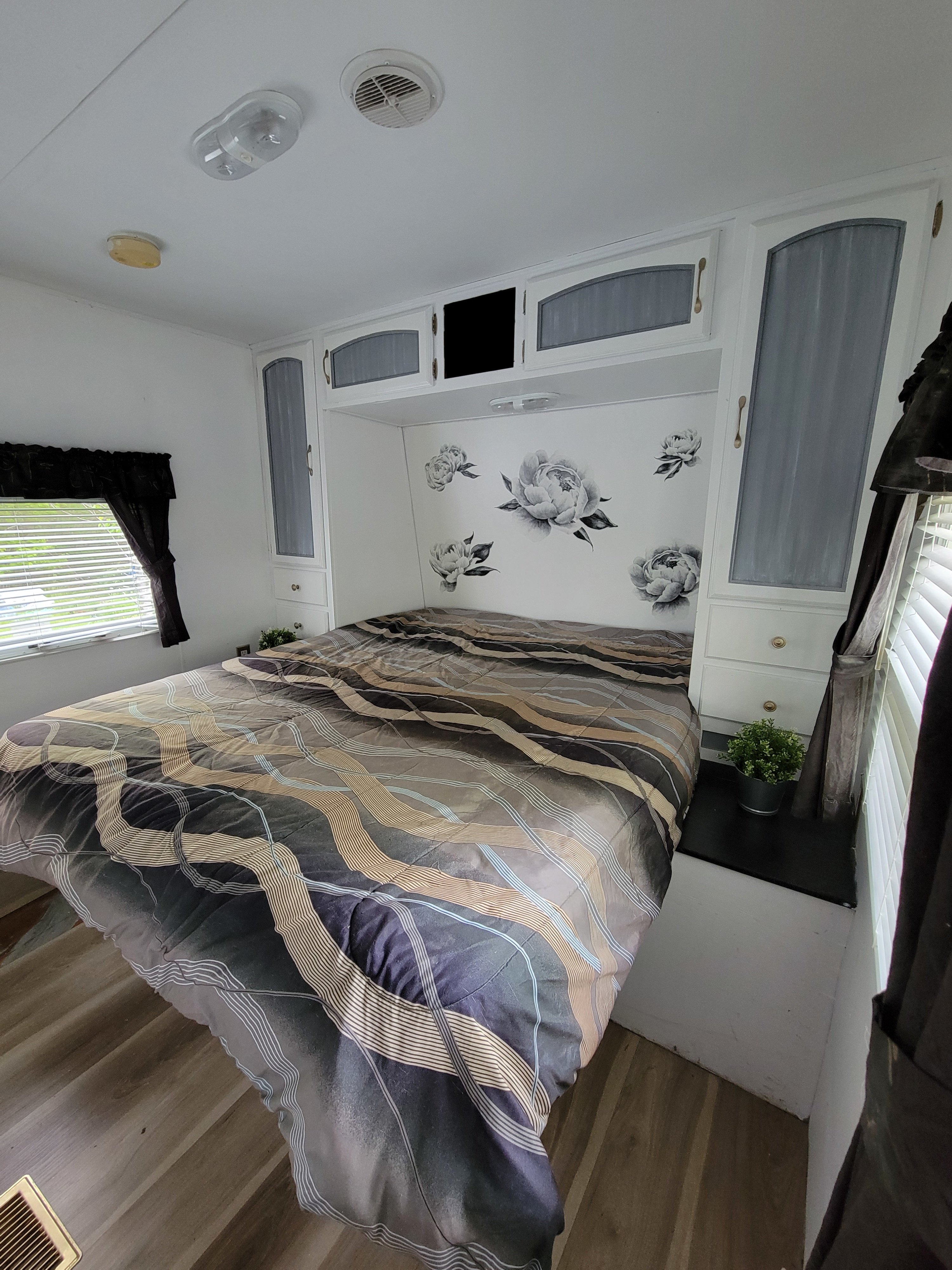 Comfortable RV rental bedroom with patterned bed, built-in storage, and floral wall decals. Bright and compact space.. Forest River Wildwood LE 2009