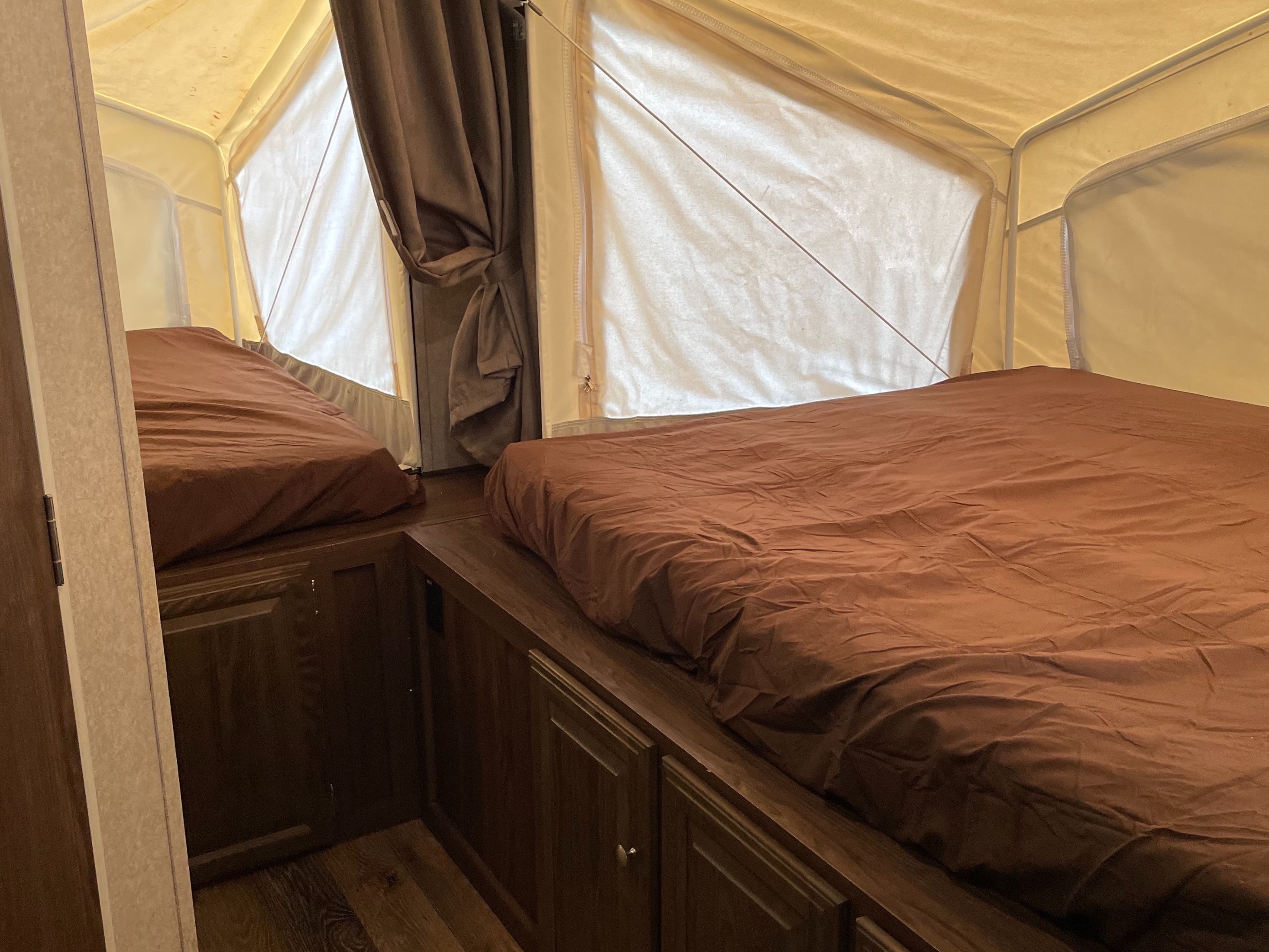 Interior of an rv rental, showing two beds with brown bedding and light canvas pop-out walls, creating a comfortable sleeping area.. Forest River Rockwood Roo 2016
