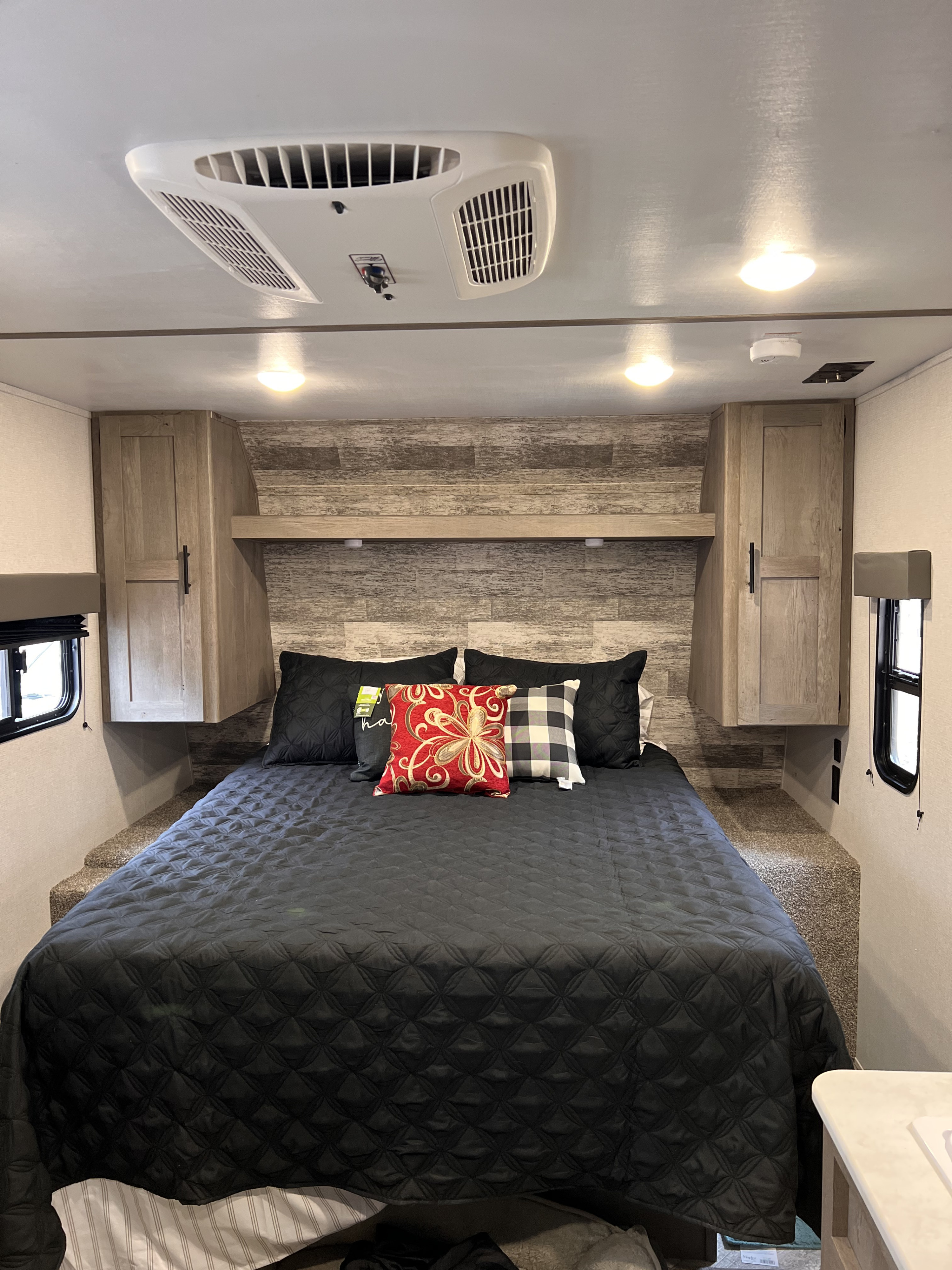Inside an RV rental bedroom: a comfy bed with black quilt, pillows, storage, AC unit, and bright ceiling lights.. Keystone RV Springdale 2021