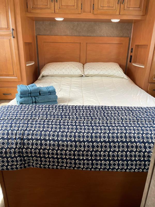 Relax in this cozy RV rental bedroom. Features a comfortable bed with pillows, a patterned blanket, and fresh blue towels.. Sunseeker 2650 2015