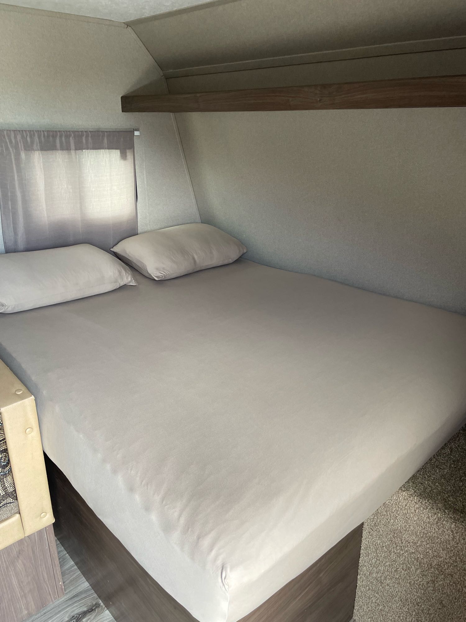 An inviting RV rental bedroom featuring a bed with light grey sheets, two pillows, and a side window.. Keystone Hideout 2018