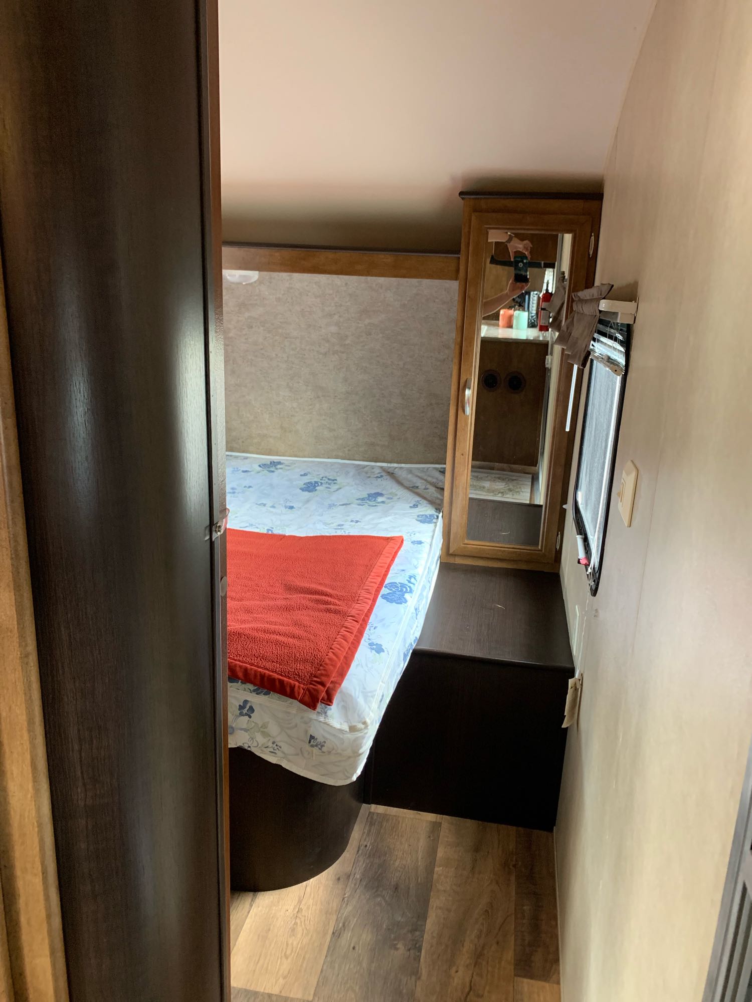 Step inside this RV rental bedroom: bed with floral sheet, orange blanket, mirrored cabinet, and window view.. Forest River Wildwood X-Lite 2016