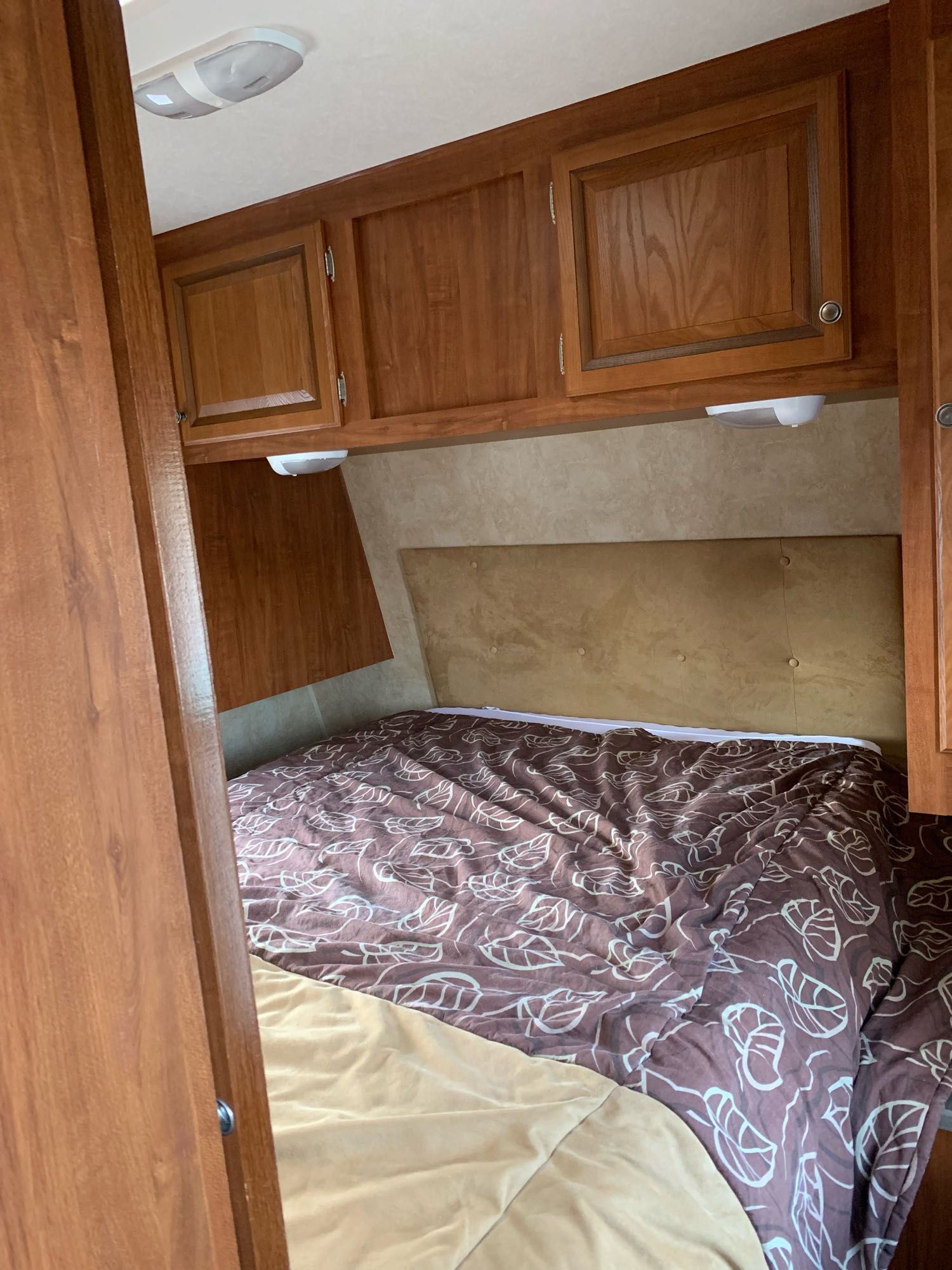 Inside an RV rental: a cozy bedroom setup with a patterned comforter, brown headboard, and storage cabinets.. Jayco Eagle Super Lite 2012