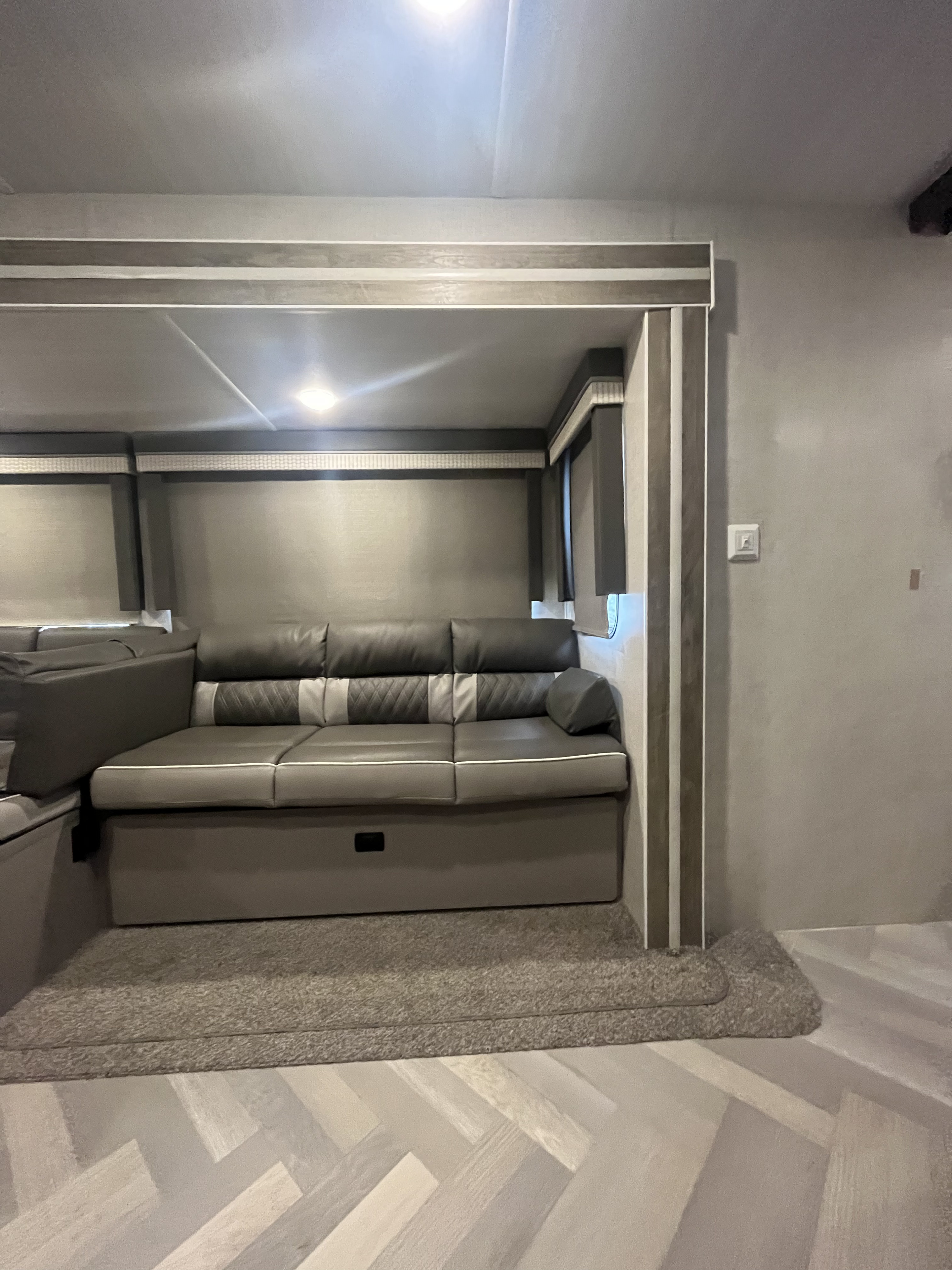 Modern gray sectional sofa inside an RV rental. Features a comfortable living area with light herringbone flooring & carpet.. Forest River Salem 2021