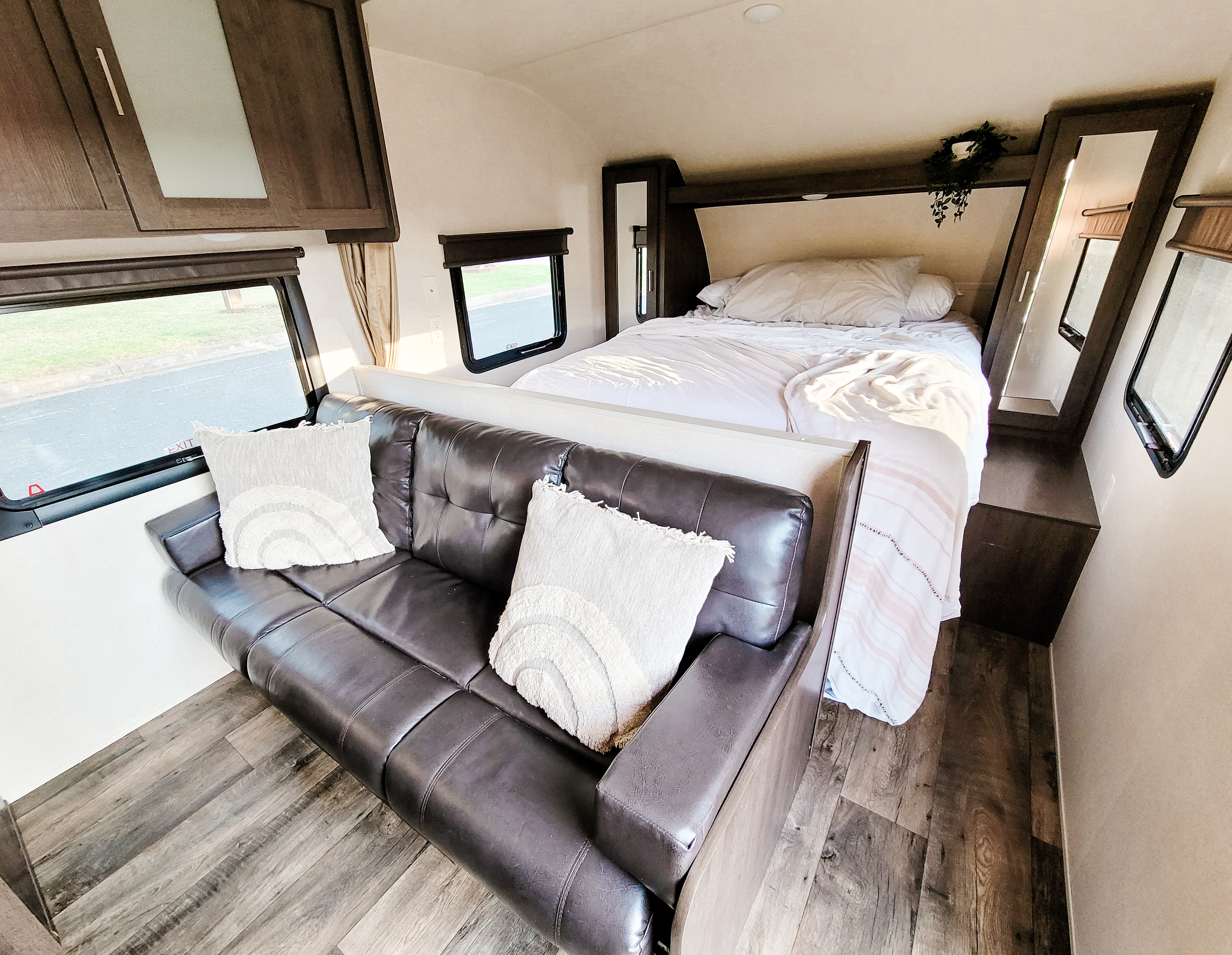 Inside a cozy RV rental: a dark sofa with pillows in the foreground, leading to a comfortable bed, wood-look floor, and bright windows.. Forest River Salem Cruise Lite 2018