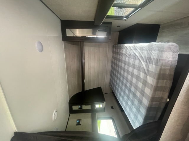 An RV rental bedroom with a grey and white plaid bed, built-in black storage units, and a ceiling window offering natural light.. Other Other 2022