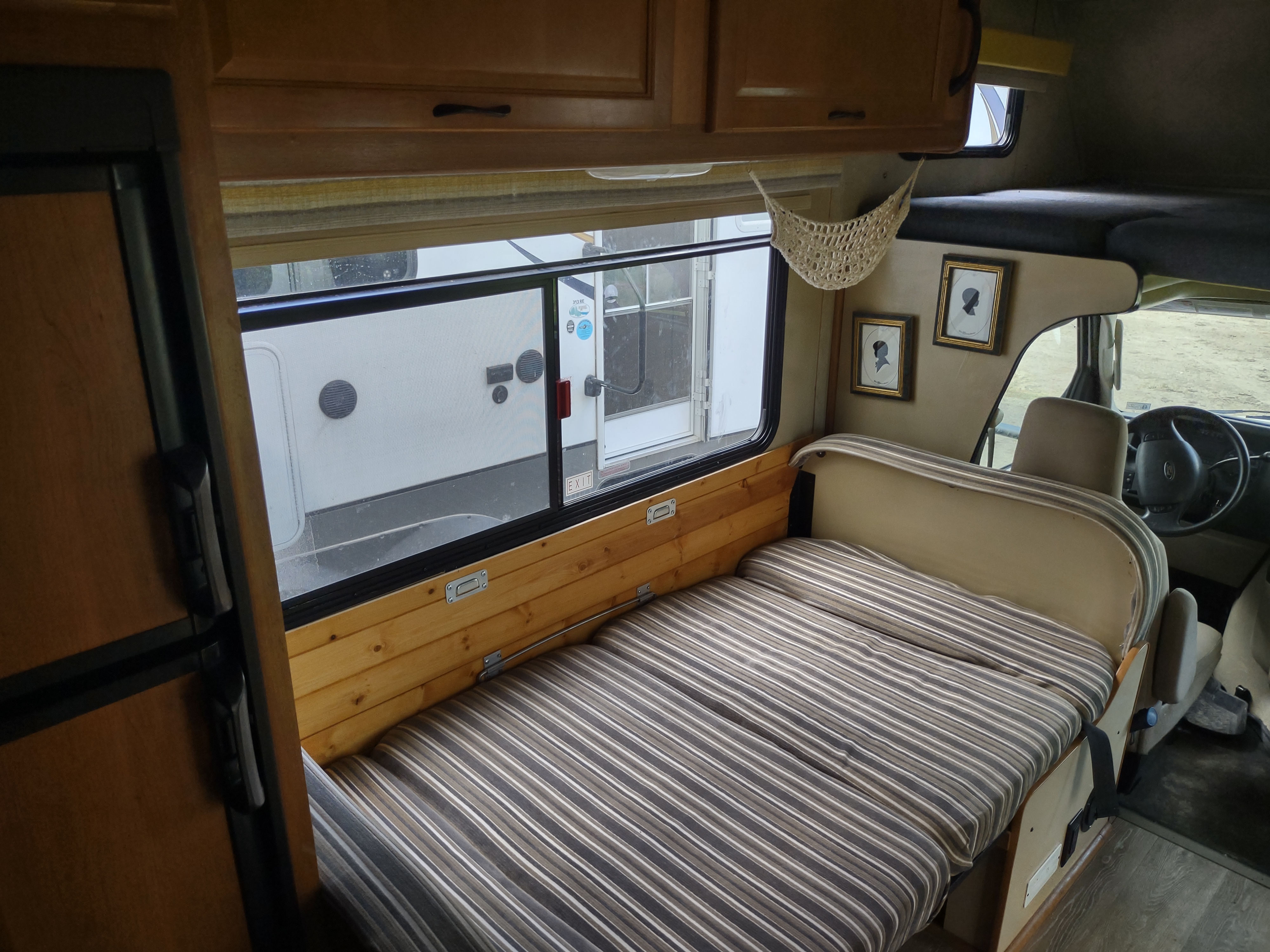 Interior of an RV rental: striped bed/seating, wood details, large window, and cabinets for a cozy travel space.. Thor Four Winds 2013