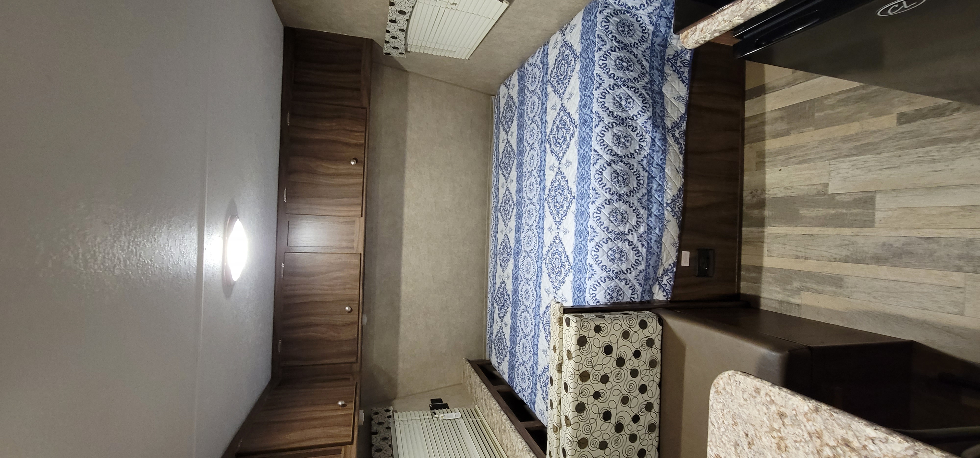 This RV rental interior features a cozy bed with a blue quilt, wood cabinets, and wood-look flooring.. Clipper Cadet 2019