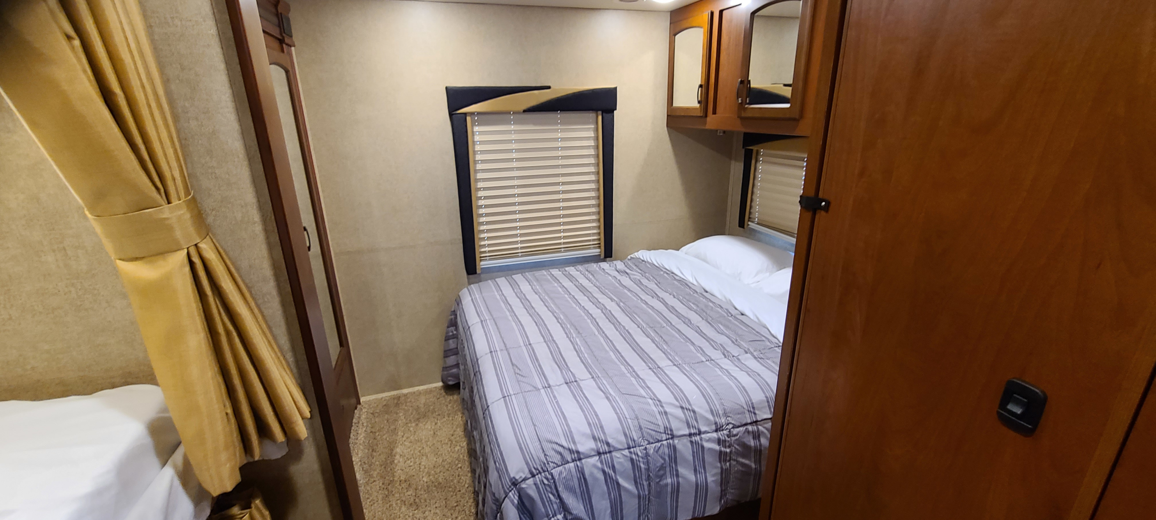 Cozy RV rental bedroom with striped bed, window blinds, mirrored cabinets, and golden curtains.. Jayco Greyhawk 2015