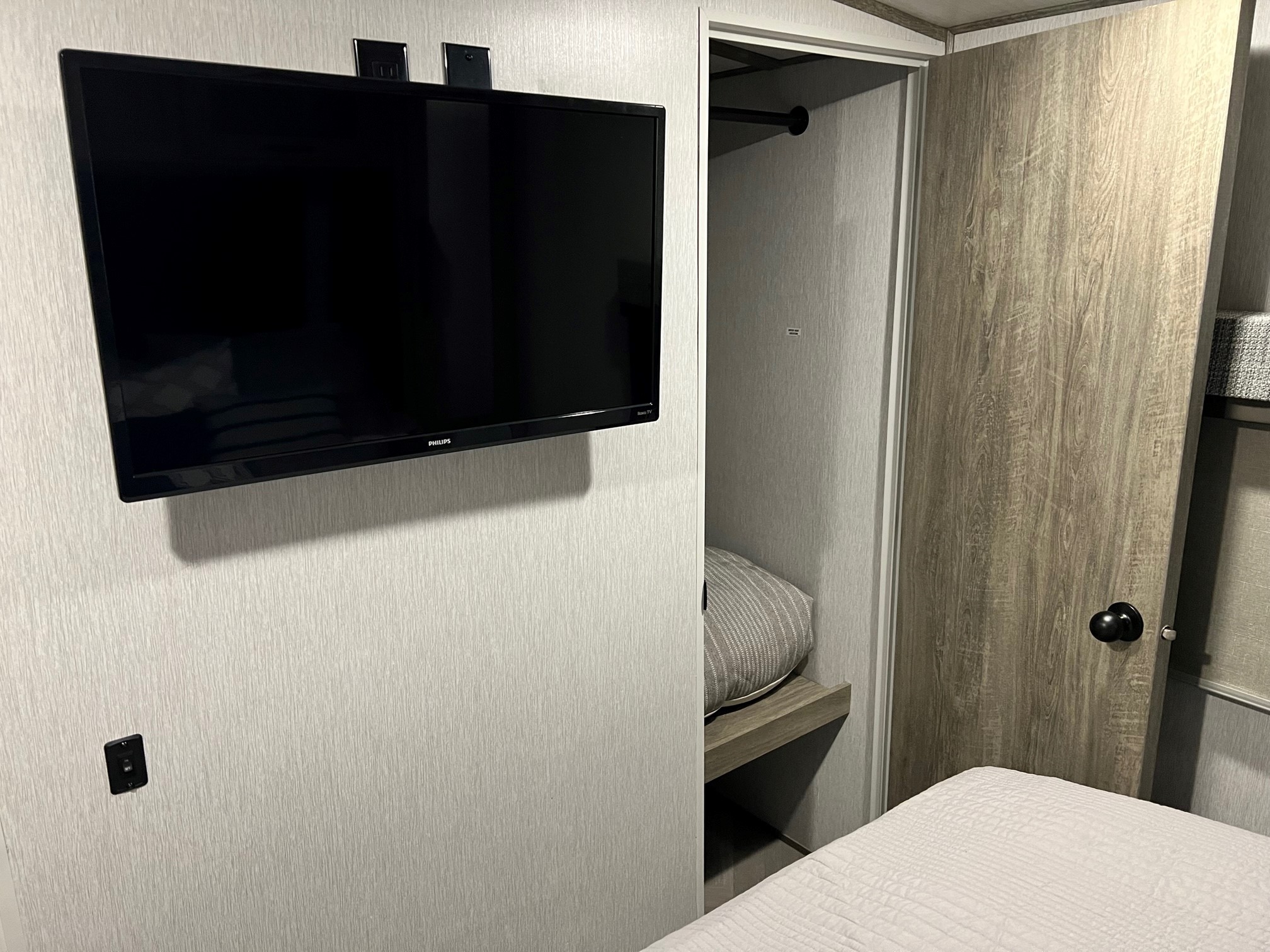 Inside an RV rental: Compact bedroom featuring a wall-mounted Philips TV, open closet with a hanging rod, and a comfy bed.. Forest River Salem Hemisphere 2022