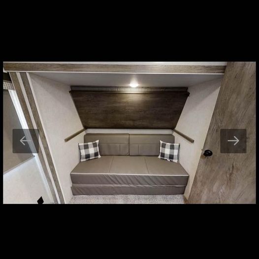 Cozy RV rental bunk area: gray sofa bed with plaid pillows, under a dark wood panel.. Forest River Wildwood 2021