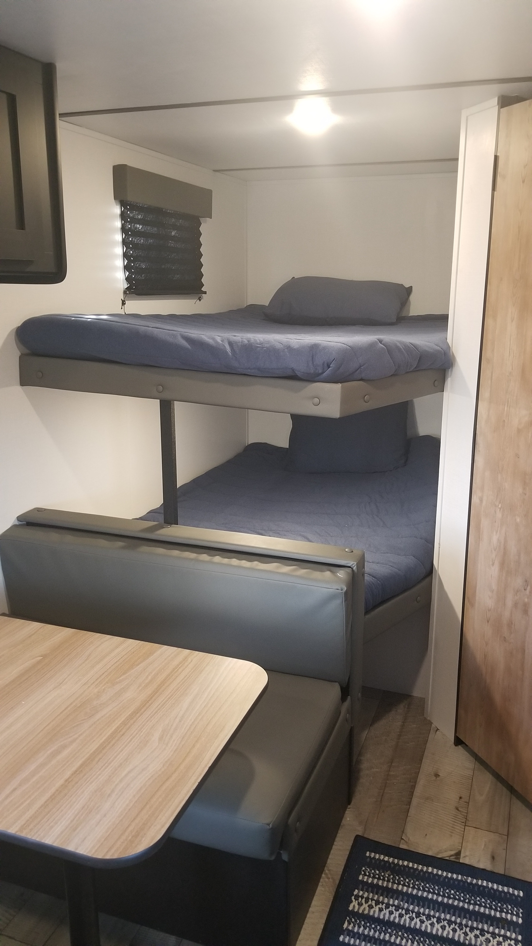 Inside an rv rental: dual bunk beds with blue mattresses and pillows, beside a grey dinette with a light wood table.. Keystone RV Springdale 2022