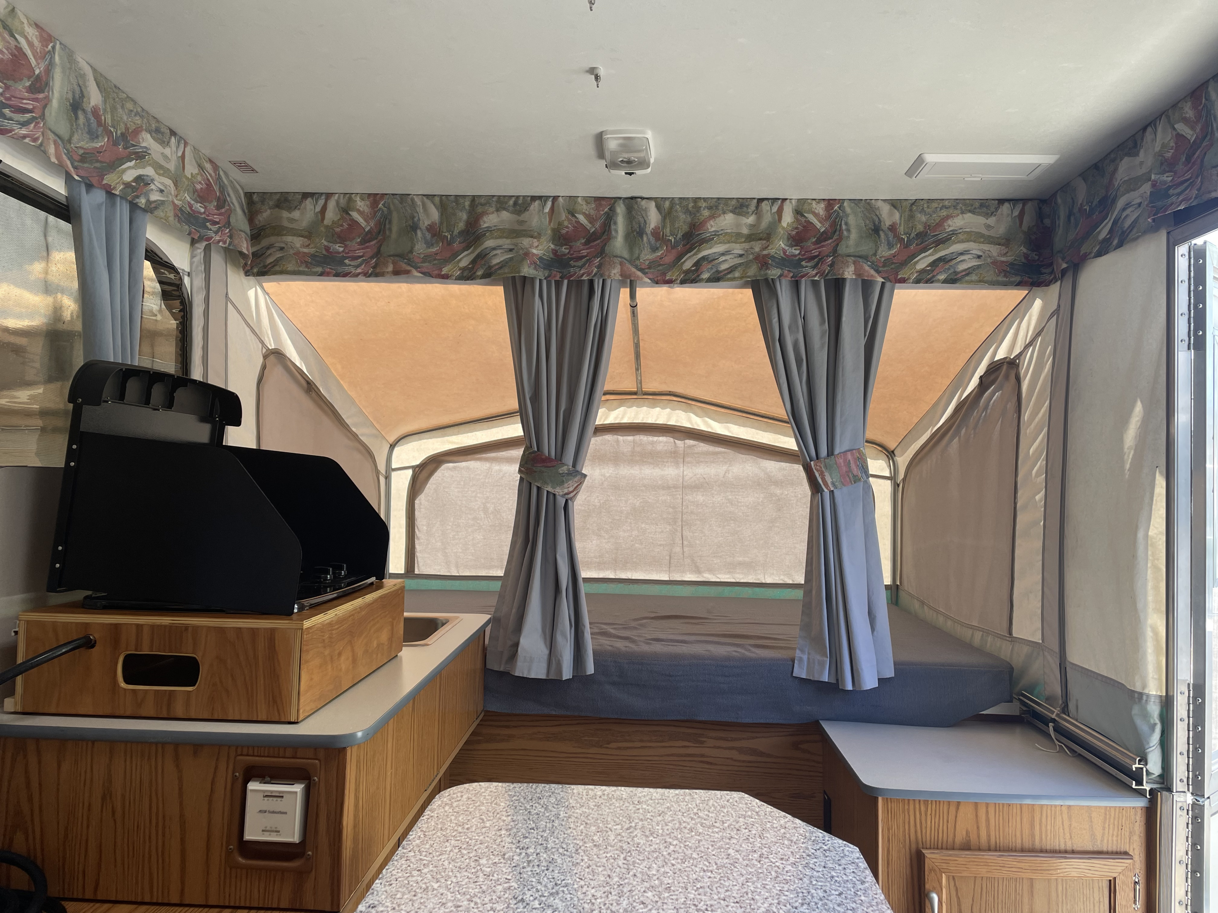 Inside a spacious pop-up RV rental, featuring a cozy bed area, compact kitchen, and dinette. Perfect for adventure.. Starcraft Venture 1999