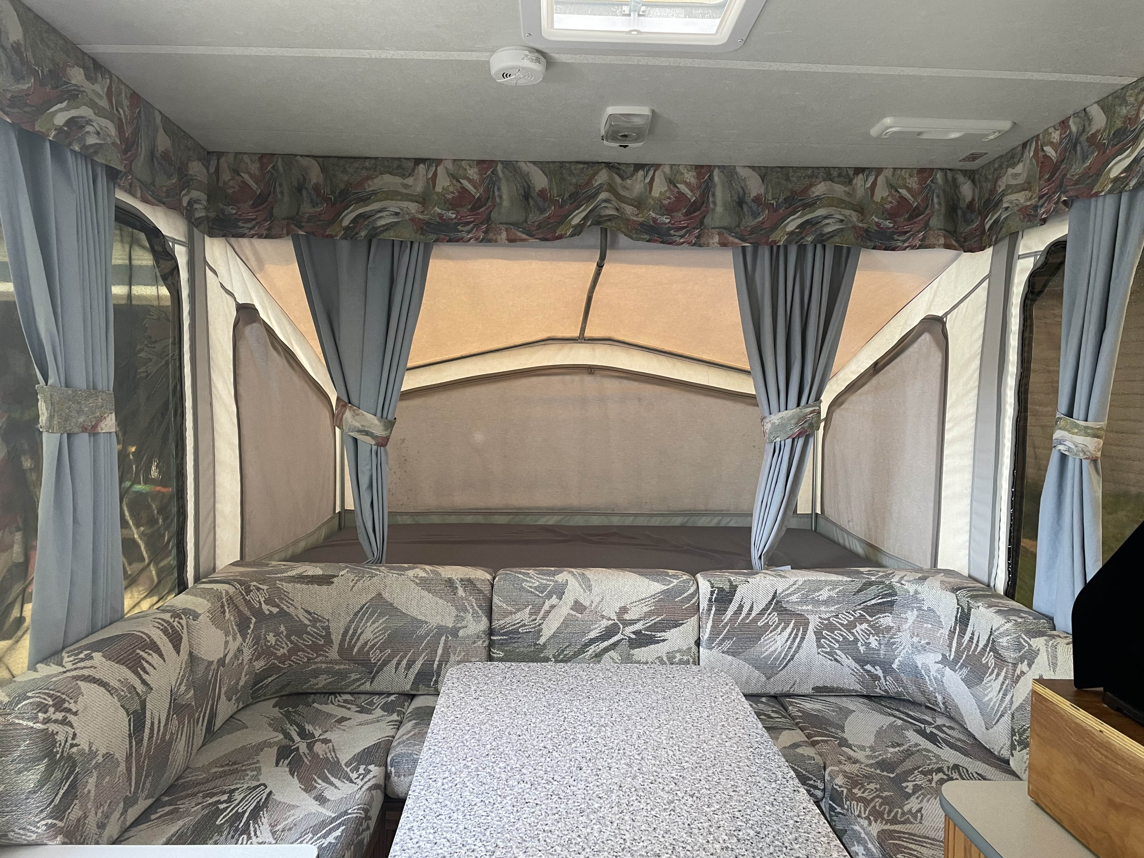 Pop-up camper rv rental interior: U-shaped seating, dining table, and extended bed areas with tie-back curtains.. Starcraft Venture 1999