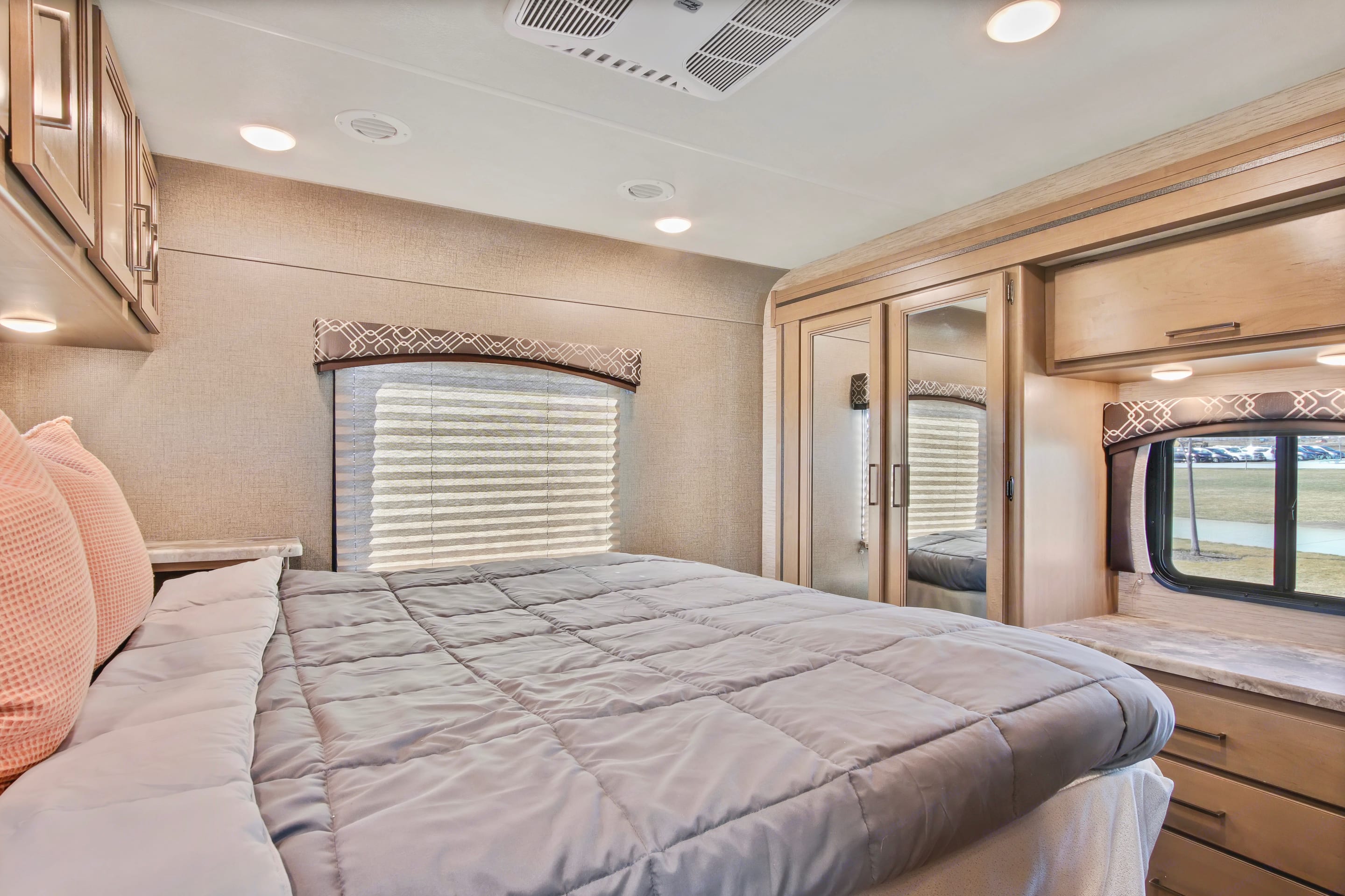 Comfortable RV rental bedroom featuring a cozy bed, modern wood cabinetry, mirrored closet, and a window for scenic views.. Thor Chateau 2021