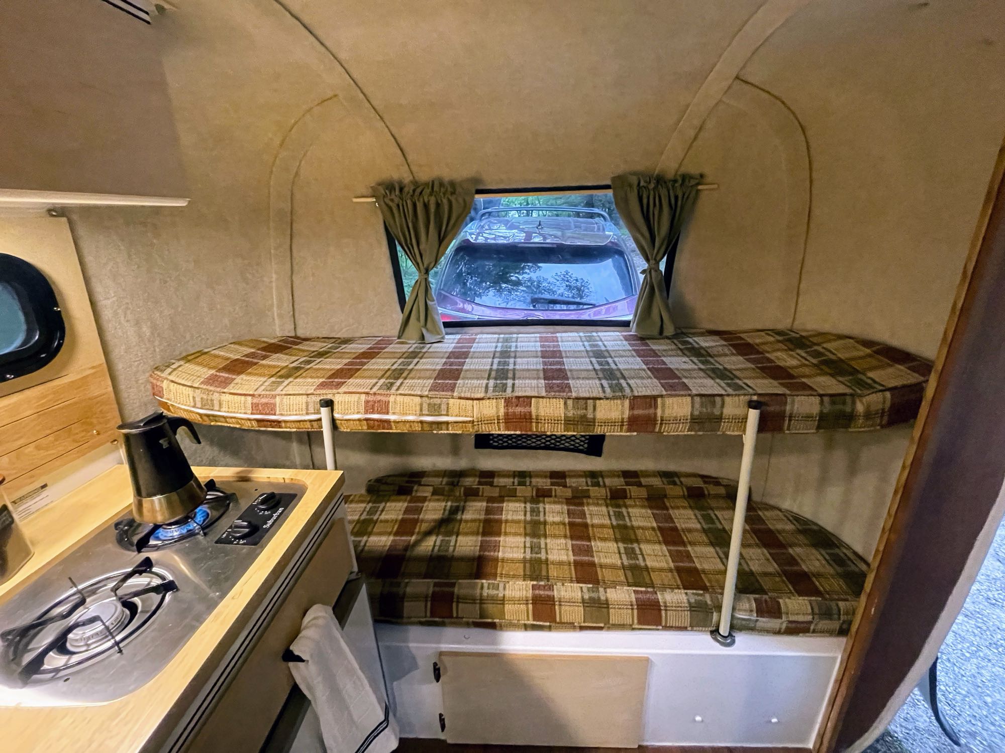Inside a compact RV rental, featuring a functional kitchen with a stove and cozy bunk beds with plaid cushions.. Scamp Scamp Trailer 2007