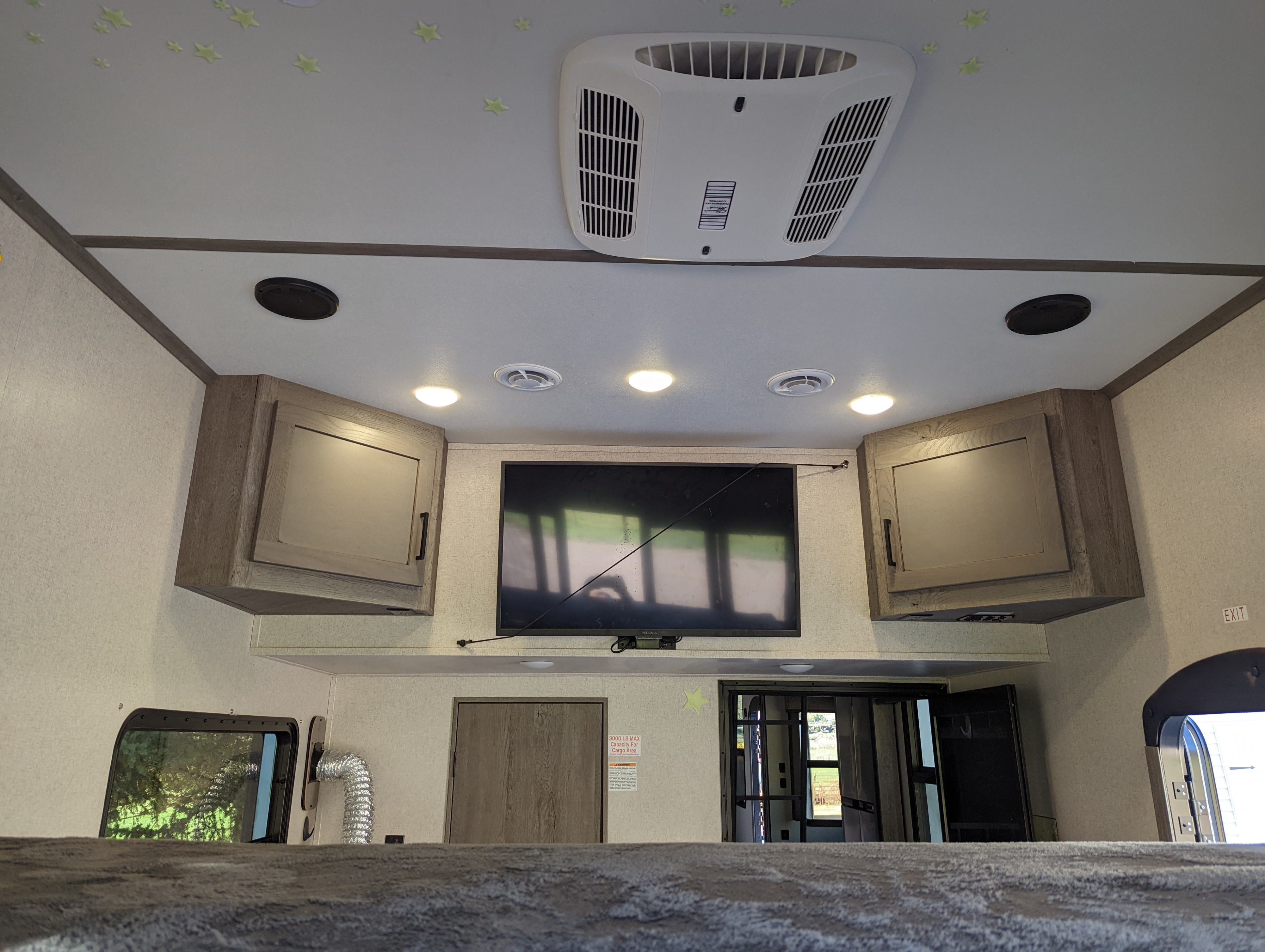 Interior of an RV rental, showing a ceiling AC unit, TV, cabinets, and doors, with glow-in-the-dark stars.. Keystone Raptor 2021