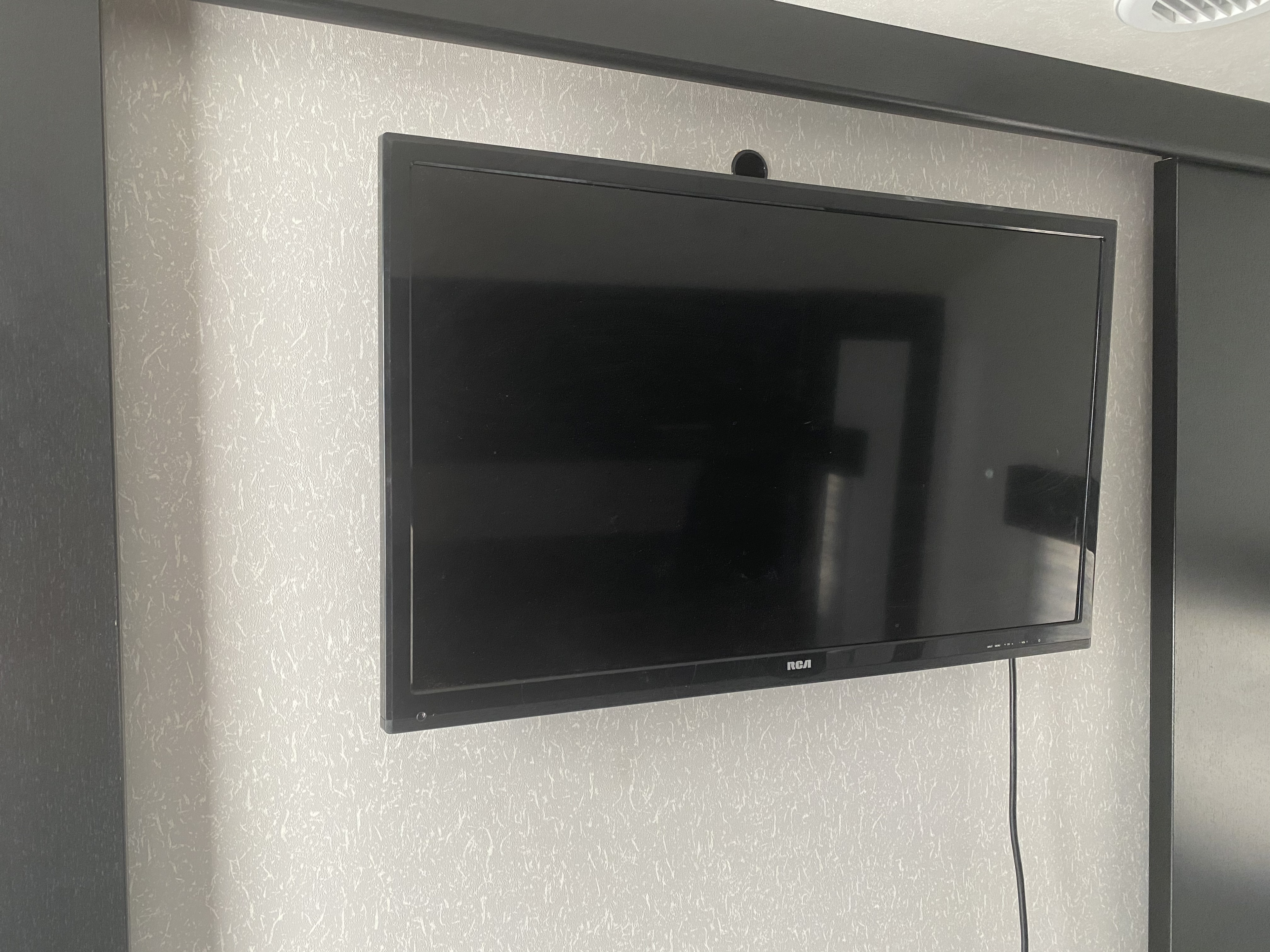 Interior view of an rv rental showing a wall-mounted RCA TV, textured light-grey wall, and dark cabinetry.. Forest River Cherokee Grey Wolf 2022