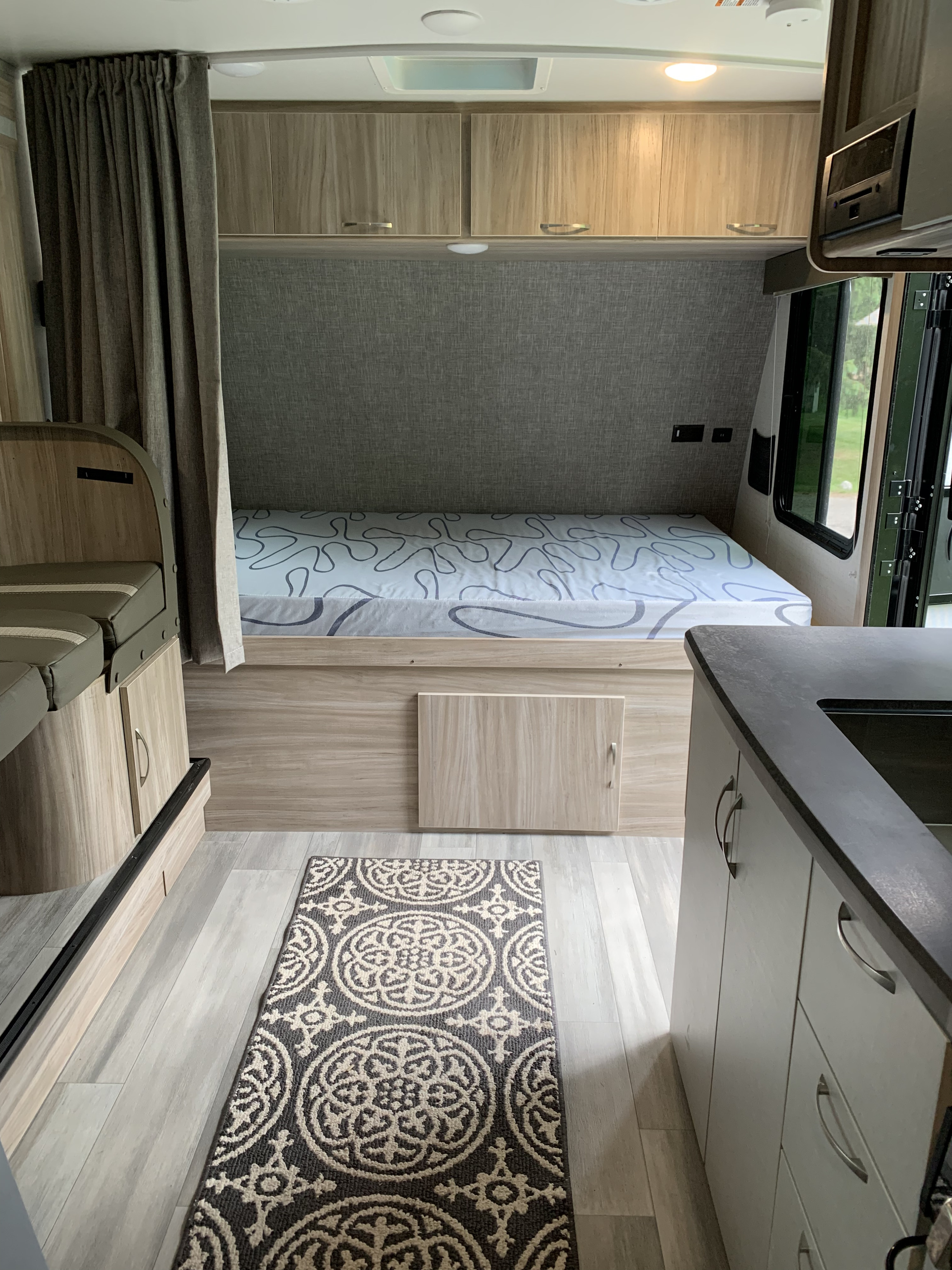 Inside an RV rental: a compact bedroom with a bed & storage, plus a glimpse of the kitchen and dining area.. Winnebago Micro Minnie 2021